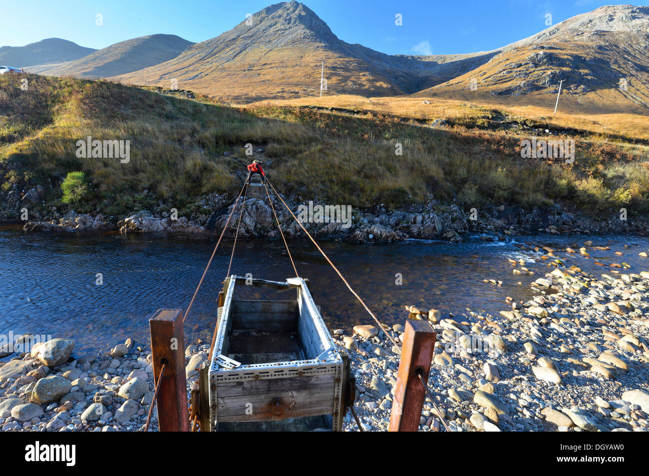 Escursionista attraversando il fiume Etive attraverso un avventuroso cavo in acciaio ponte, autunno nella valle di Glen Etive, Highlands scozzesi Foto Stock