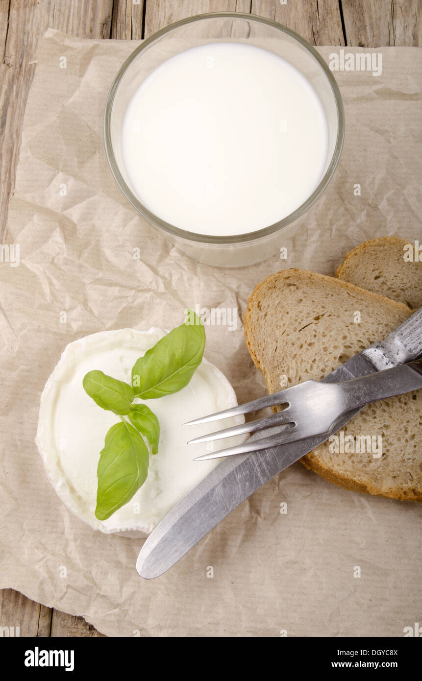 Formaggio di capra, basilico, pane e latte su una country house tavolo da cucina Foto Stock