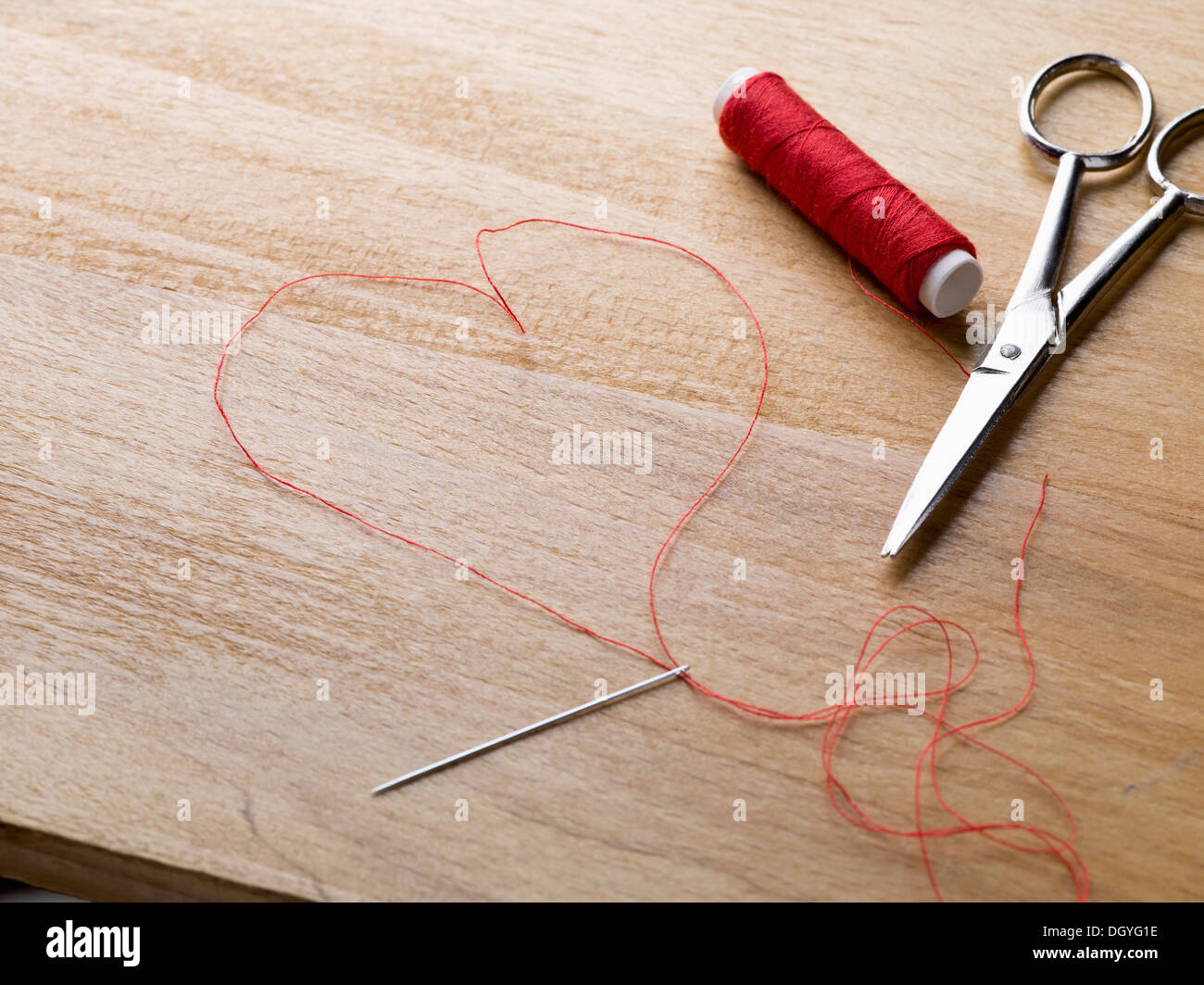 Un rocchetto di filo rosso, forbici, filo ago e filo sagomato come un cuore Foto Stock