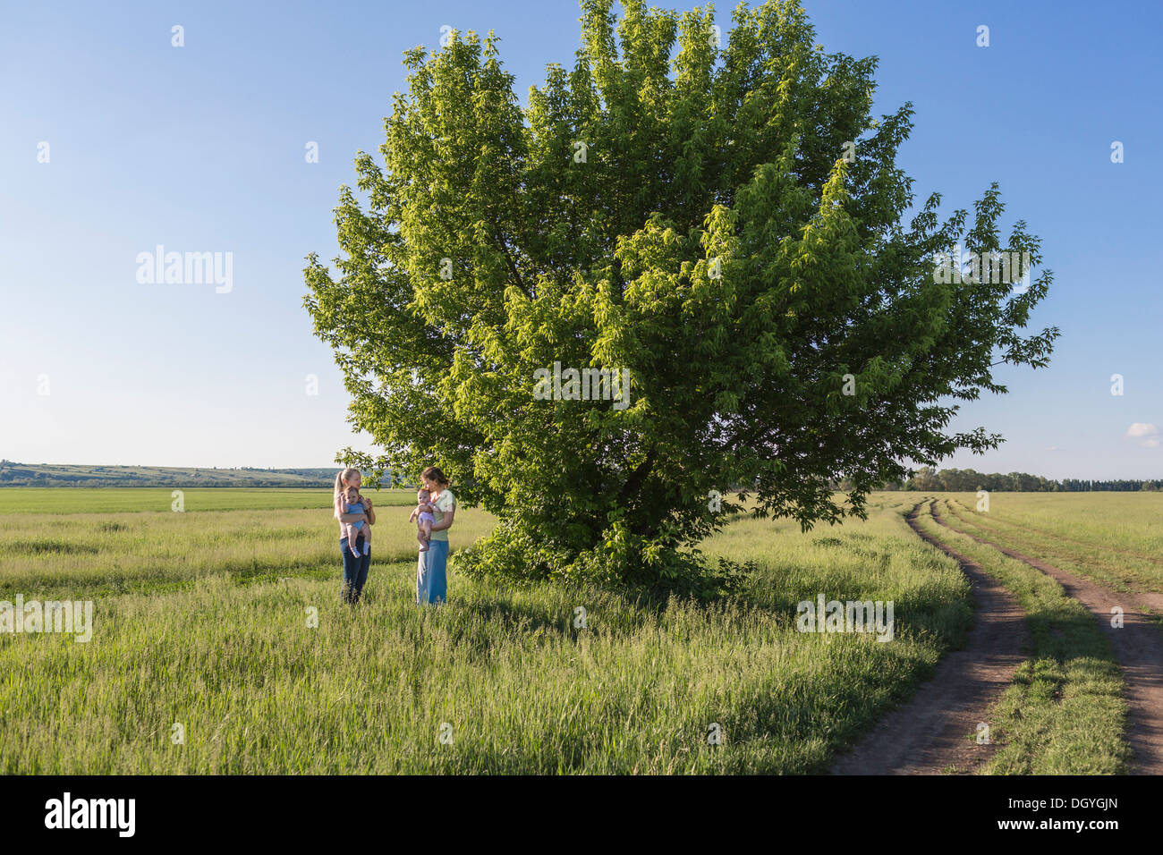 Due mamme con i loro bambini mentre in piedi in un campo Foto Stock