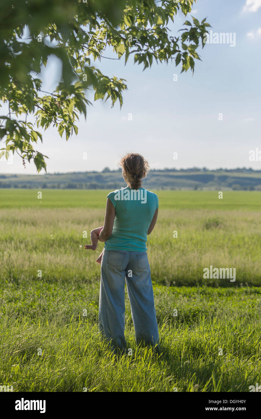 Una madre in piedi in un campo mentre si tiene il suo bambino e guardando la vista Foto Stock