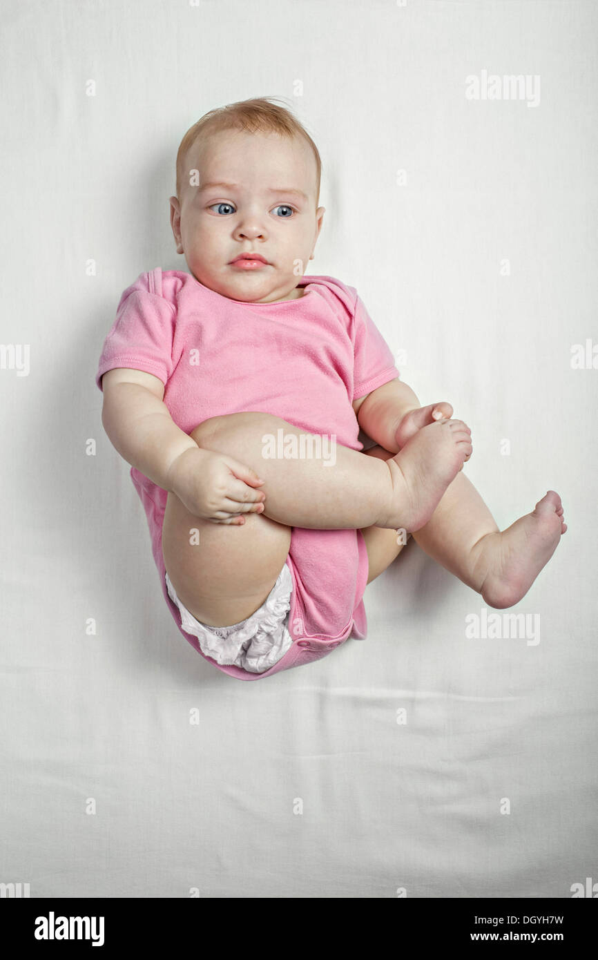 Una bambina sdraiata sulla schiena di toccare i suoi piedi nudi curiosamente Foto Stock