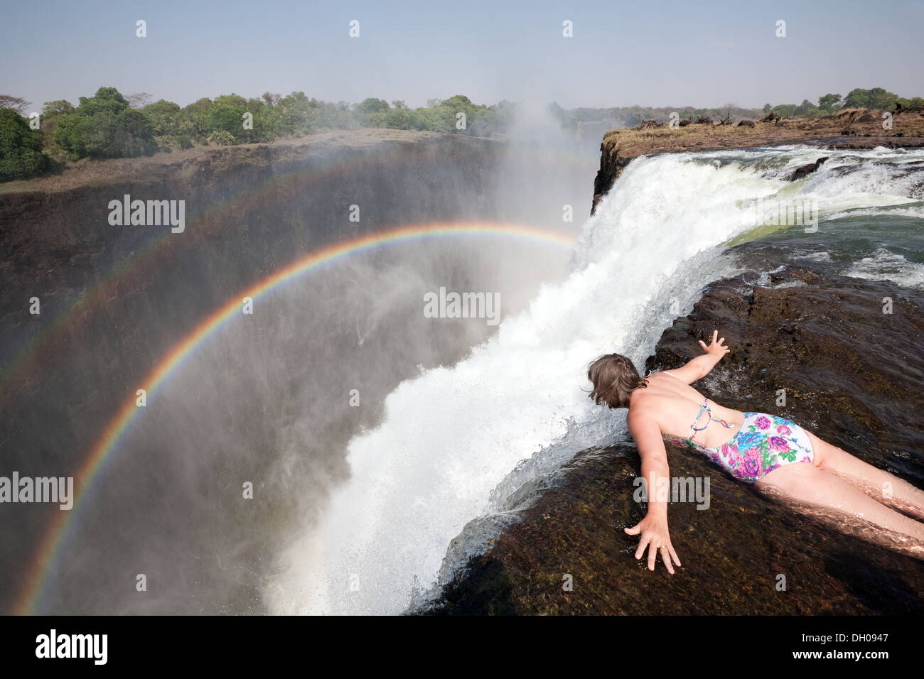 Di mezza età donna caucasica guardando oltre il bordo del Victoria Falls in pool di diavoli, esempio di vacanza avventurosa, Zambia Africa Foto Stock