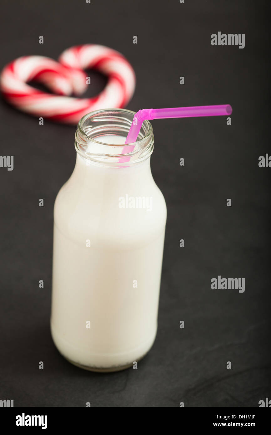 Vista dettagliata del latte in un barattolo di vetro con paglia rosa e rosso caramella cuore in background sulla superficie scura Foto Stock