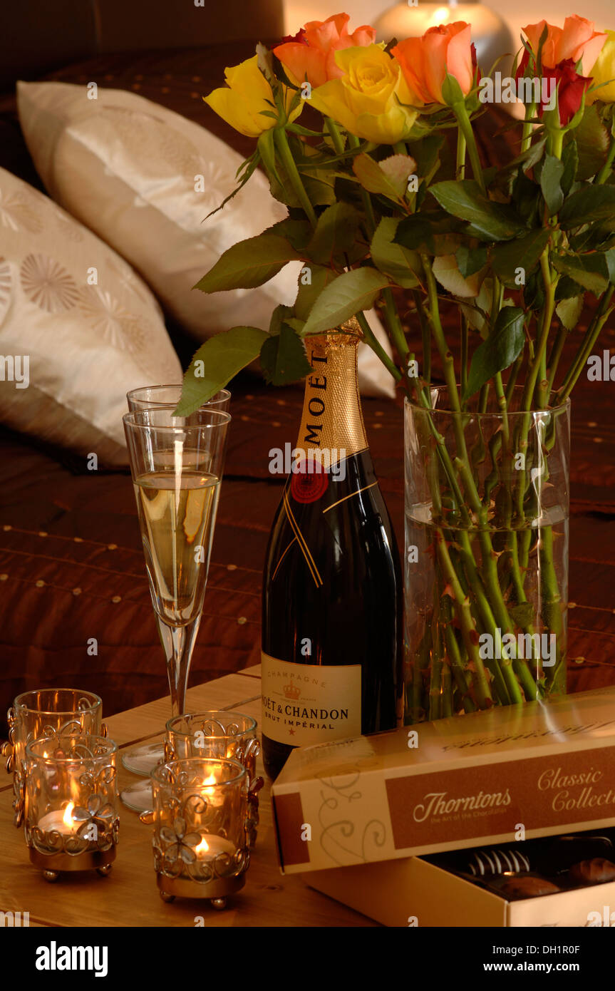 Scena romantica con due bicchieri di champagne Moet, Thorntons  cioccolatini, rose, bianco cuscini gettata su di un colore rosso scuro  trapunta Foto stock - Alamy