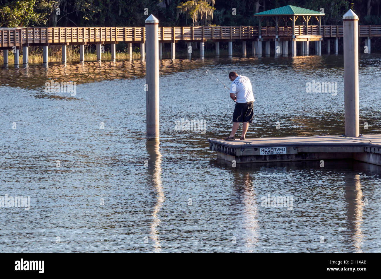L'uomo con la canna da pesca la pesca da una dock nel supporto Dora Harbour in Florida centrale, sentiero natura boardwalk visibile oltre. Foto Stock