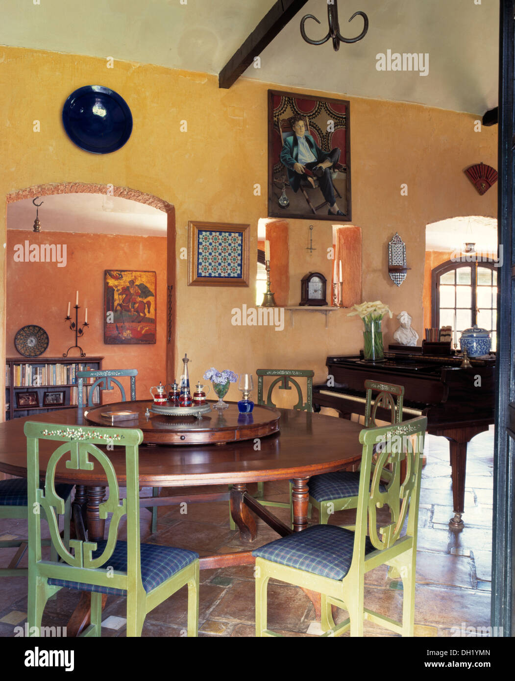 Verde pallido sedie dipinte a tavola circolare con Lazy Susan in spagnolo villa sala da pranzo con pianoforte Foto Stock