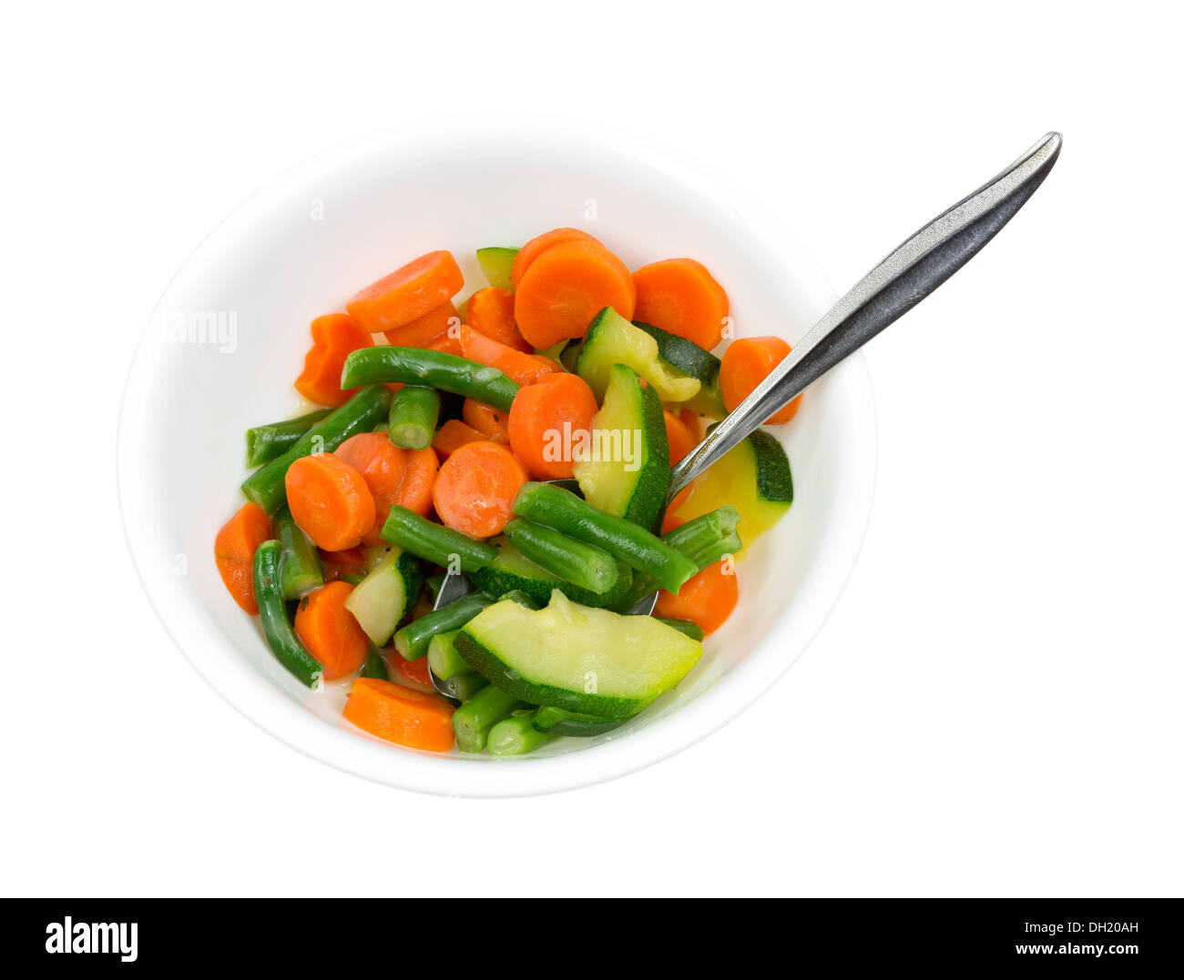 Un bianco ciotola riempita con zucchini cotto, i fagiolini e le carote in una salsa di burro con un cucchiaio. Foto Stock