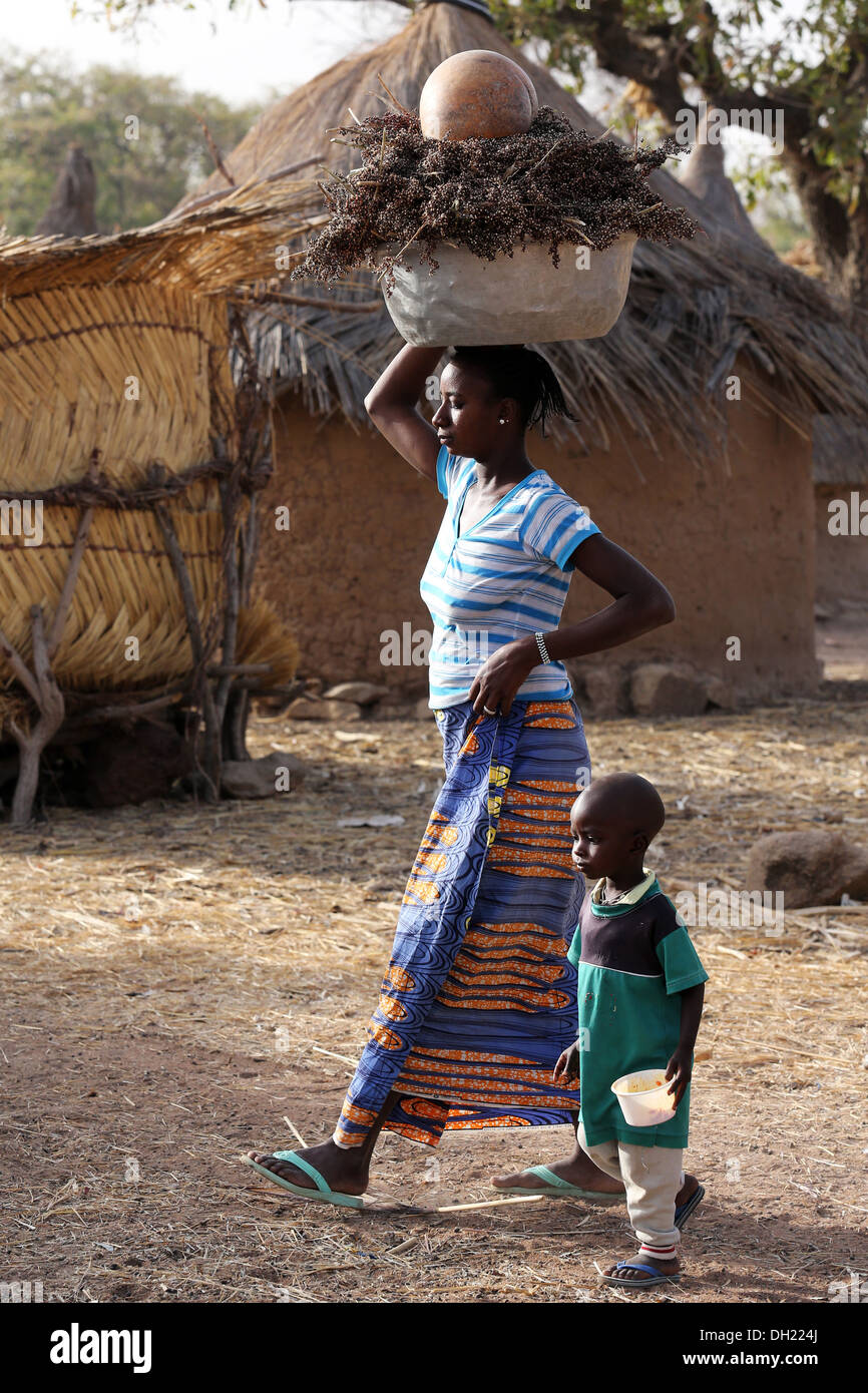 Donna che trasportano il sorgo sul suo capo con il suo bambino in un villaggio del Burkina Faso Foto Stock