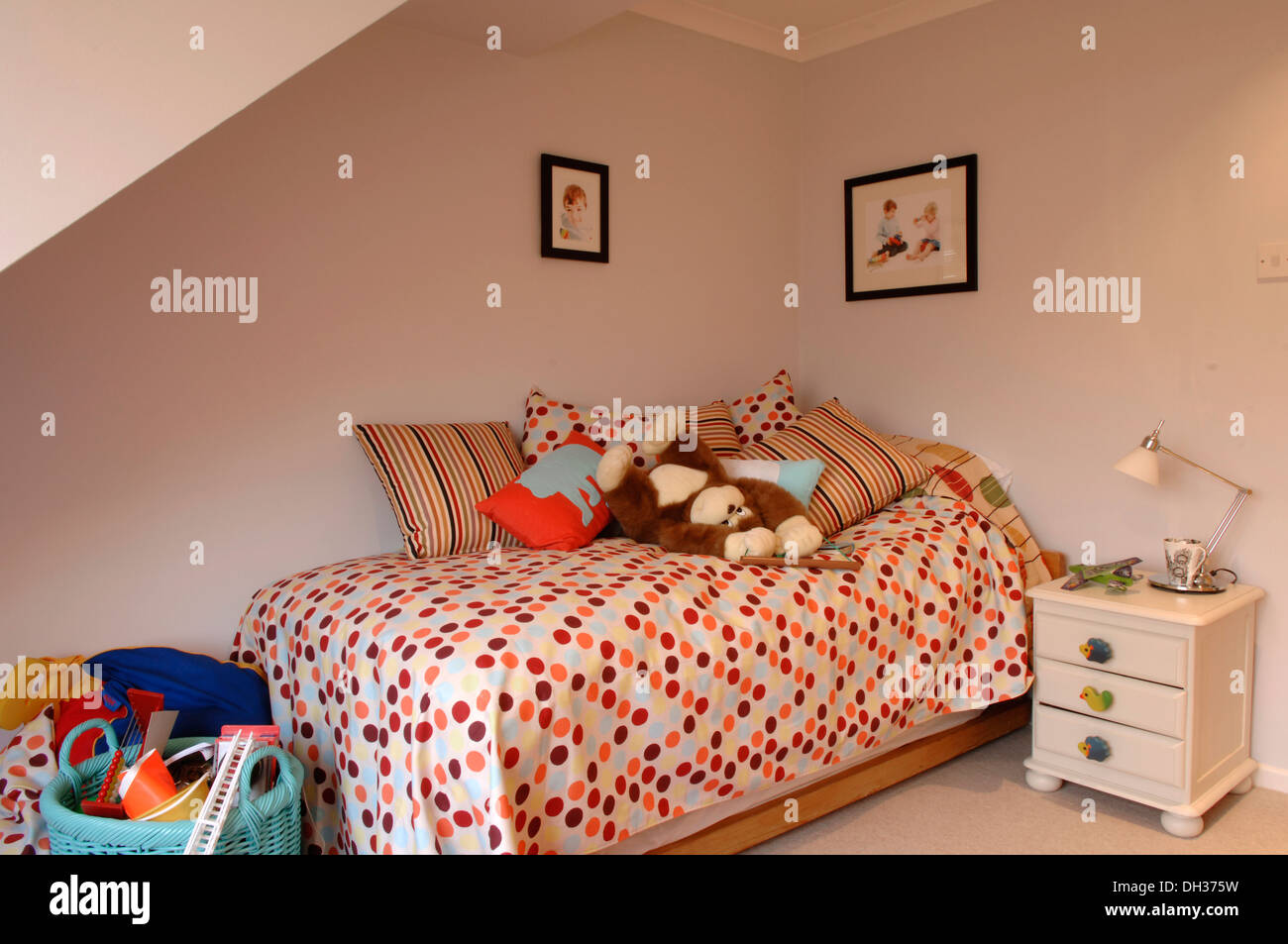 Un piccolo ma ben progettato childs camera da letto con pareti chiare e colorati di spotted quilt, piumone e cuscini bianchi nonché giocattoli morbidi Foto Stock