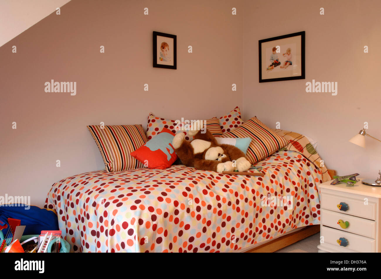 Un piccolo ma ben progettato childs camera da letto con pareti chiare e colorati di spotted quilt, piumone e cuscini bianchi nonché giocattoli morbidi Foto Stock