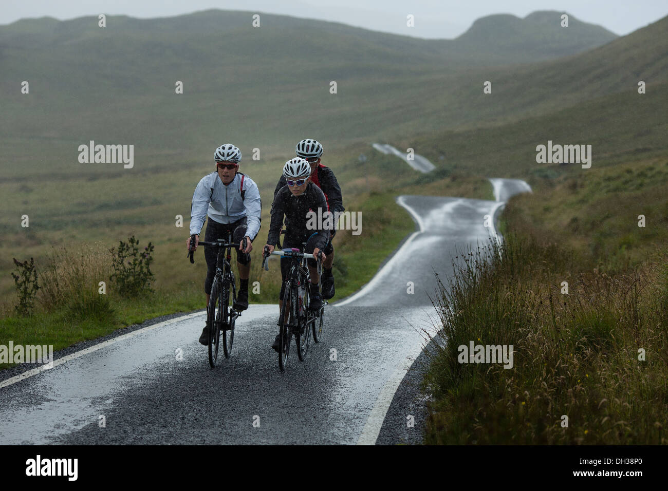 Tre i ciclisti cavalcare un percorso umido nelle Highlands scozzesi, Scotland, Regno Unito Foto Stock