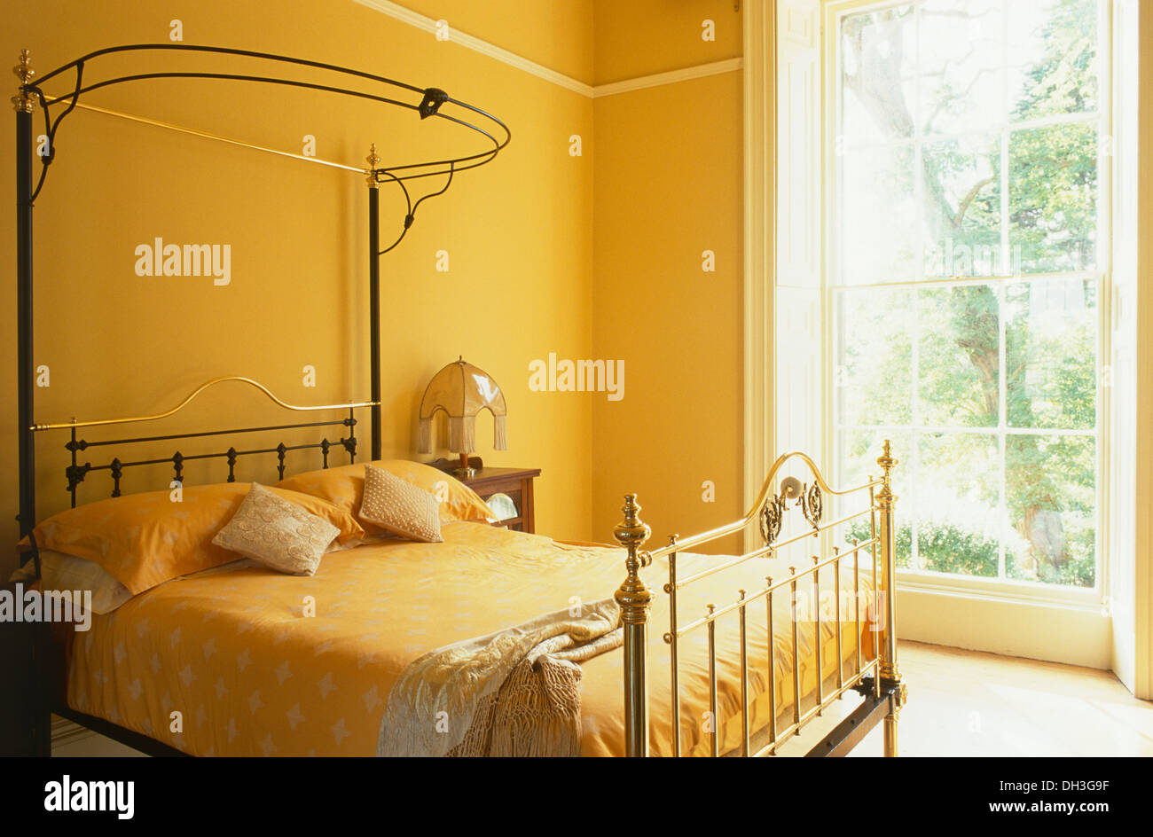 Biancheria di colore arancione e il coperchio sul tester per metà in ottone antico letto in camera da letto arancione con finestre a parete Foto Stock