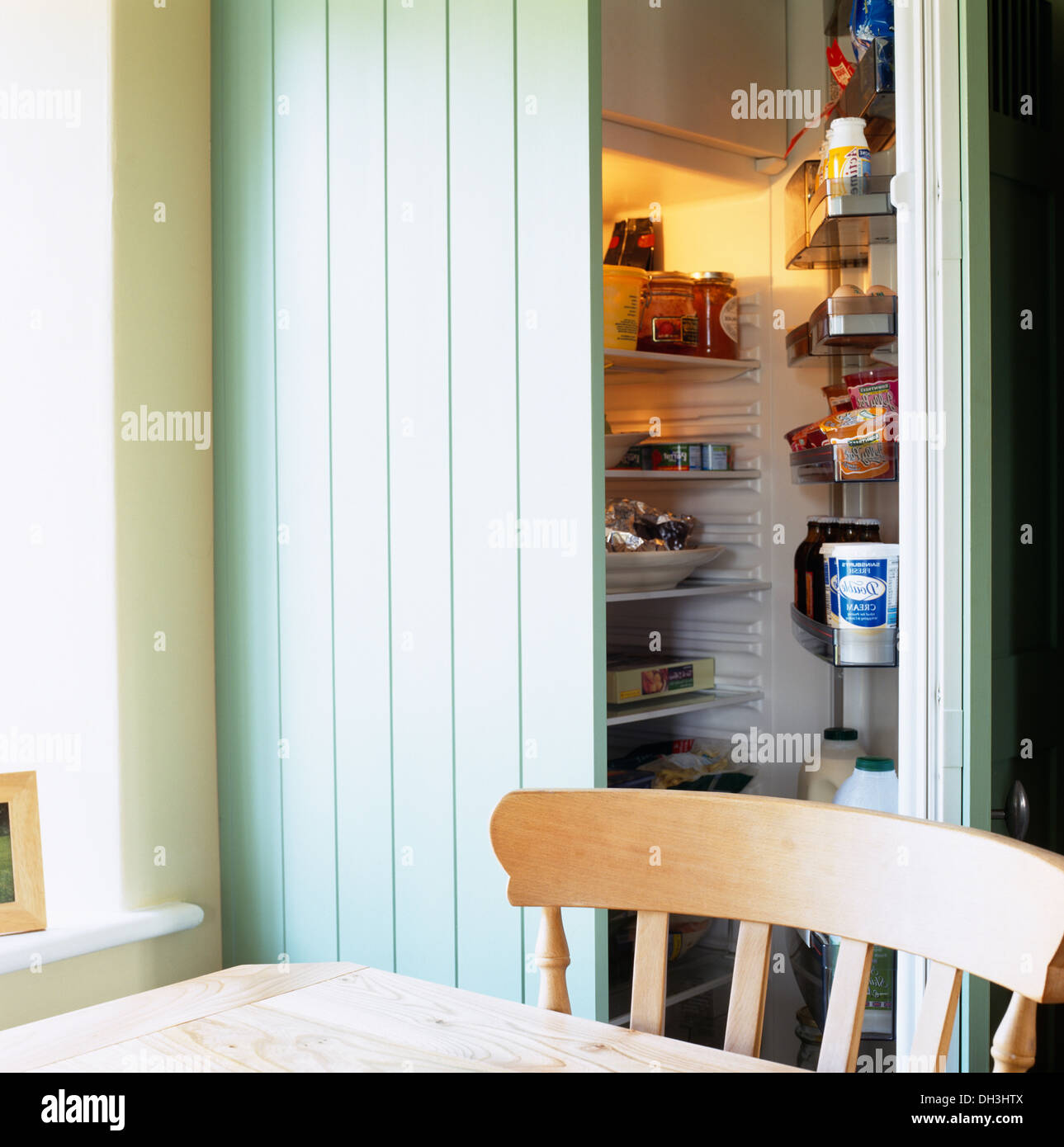 Legno pallido sedia al tavolo da cucina di fronte aqua blue porta aperta al frigo a scomparsa Foto Stock
