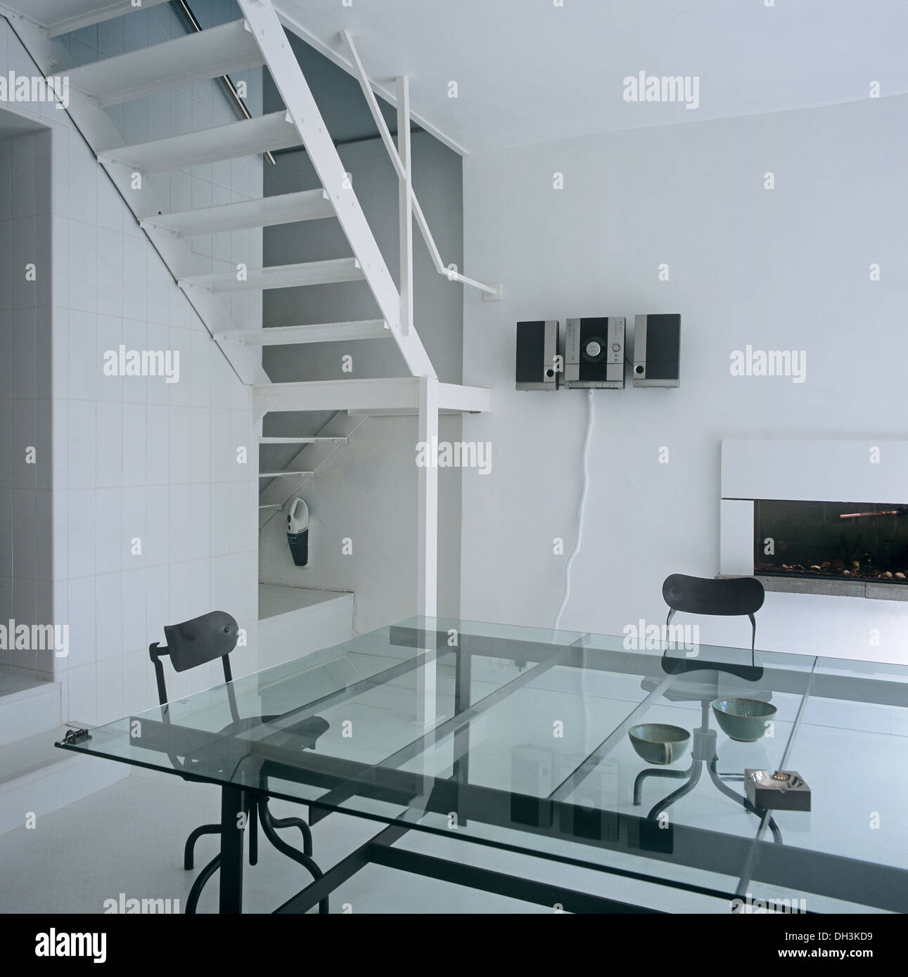 Grande tavolo in vetro e sedie nere in un piano aperto sala da pranzo moderna con metallo bianco scalinata e caminetto minimalista Foto Stock