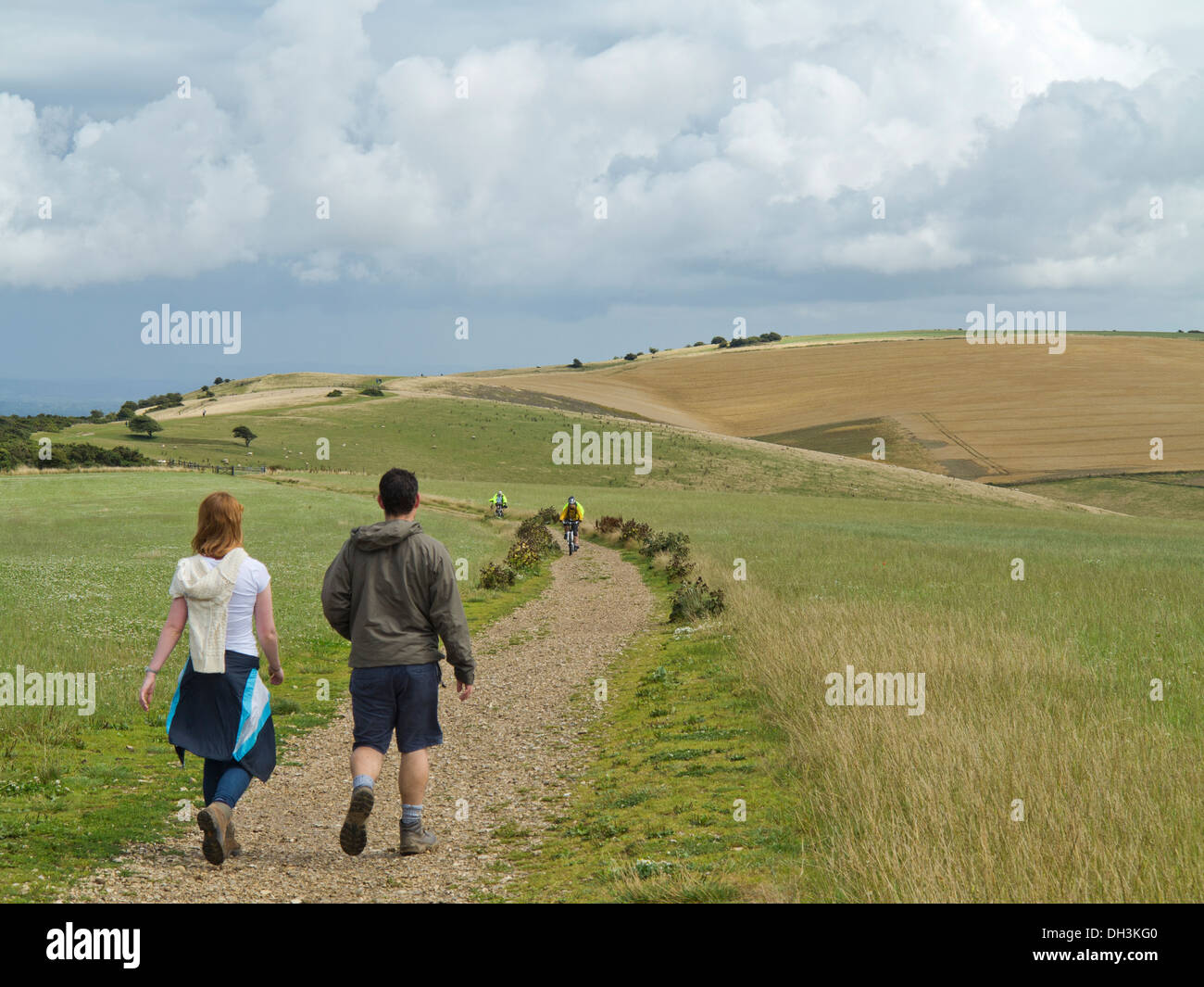 Giovane uomo e donna che cammina su South Downs sentiero vicino Ditchling Beacon Sussex con i ciclisti in background sul fine settimana estivo Foto Stock