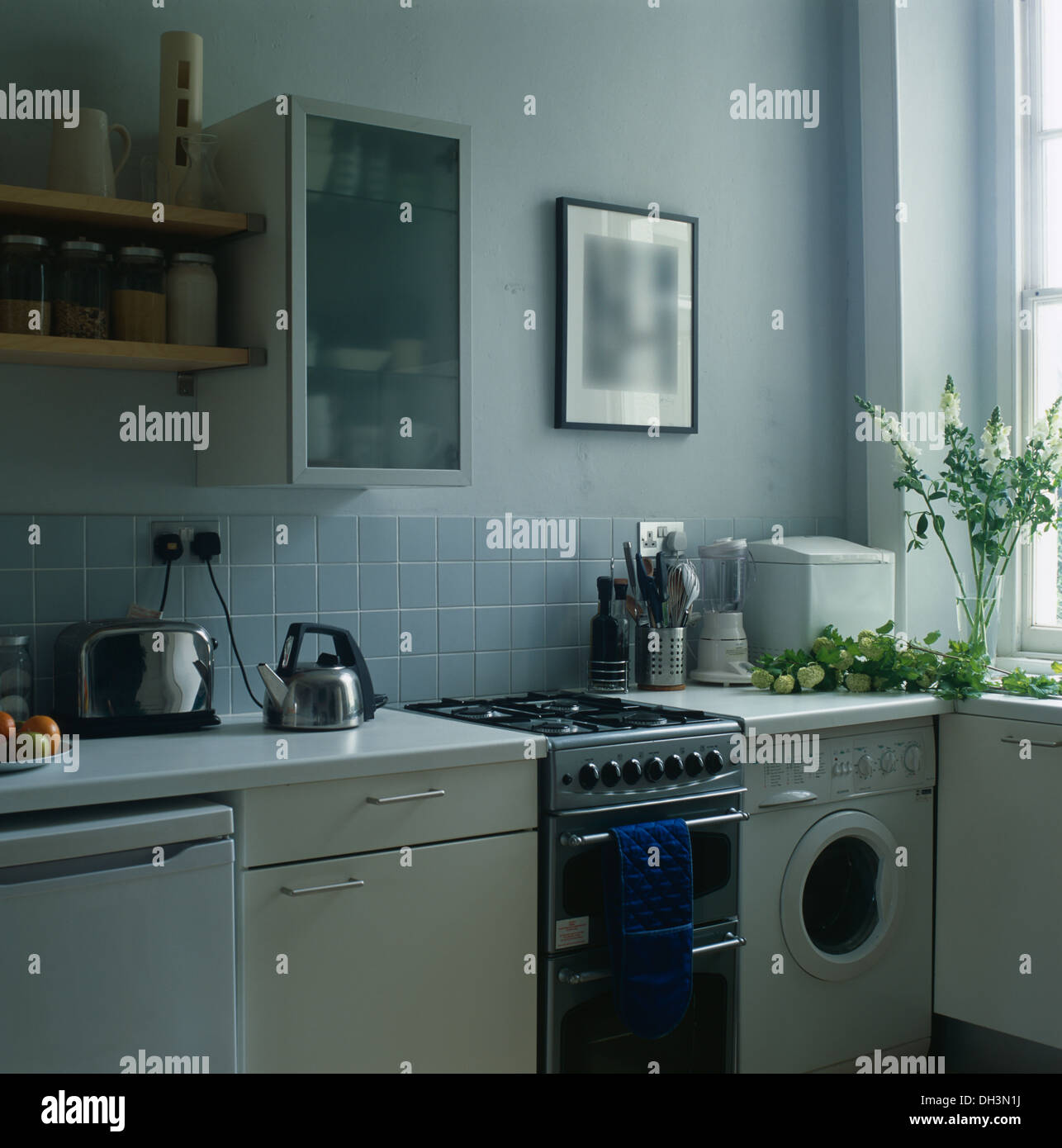 Vetro opaco cabinet anteriore sulla parete sopra forno a gas e piccola  macchina di lavaggio in blu pallido cucina con chrome un bollitore e un  tostapane Foto stock - Alamy