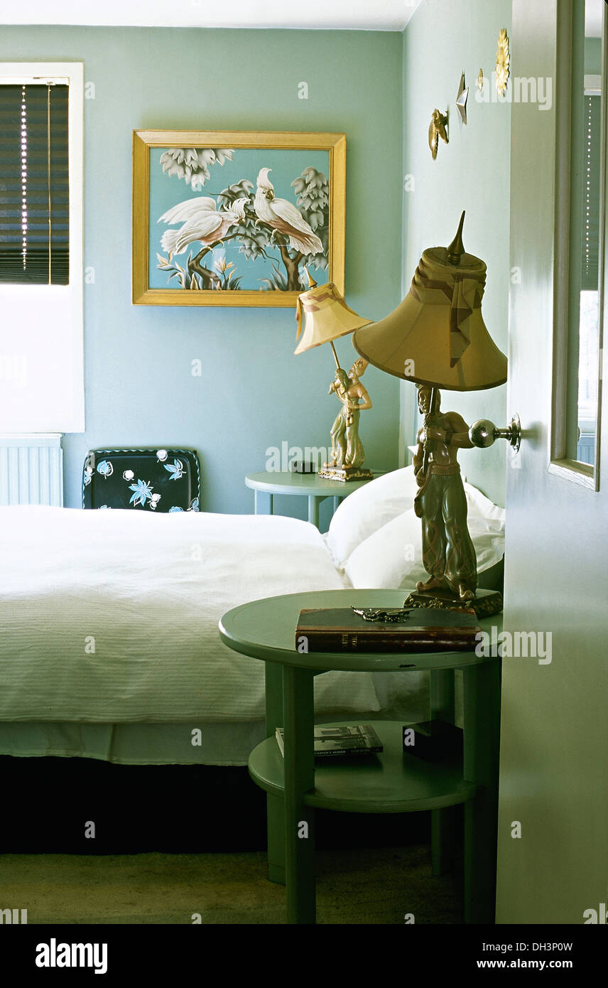 Inusuali lampade figurine sul blu pallido tabelle accanto a letto con lenzuola bianche in aqua blue camera da letto con grande immagine sulla parete Foto Stock