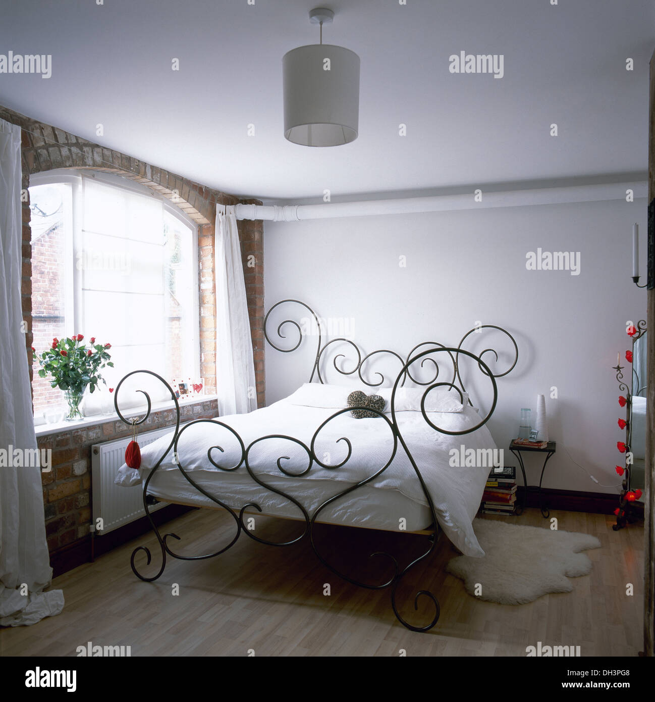 Decorativi in ferro battuto letto con lenzuola bianche in semplice bianco camera da letto con pavimento in legno e mattoni a vista parete finestra sottostante Foto Stock