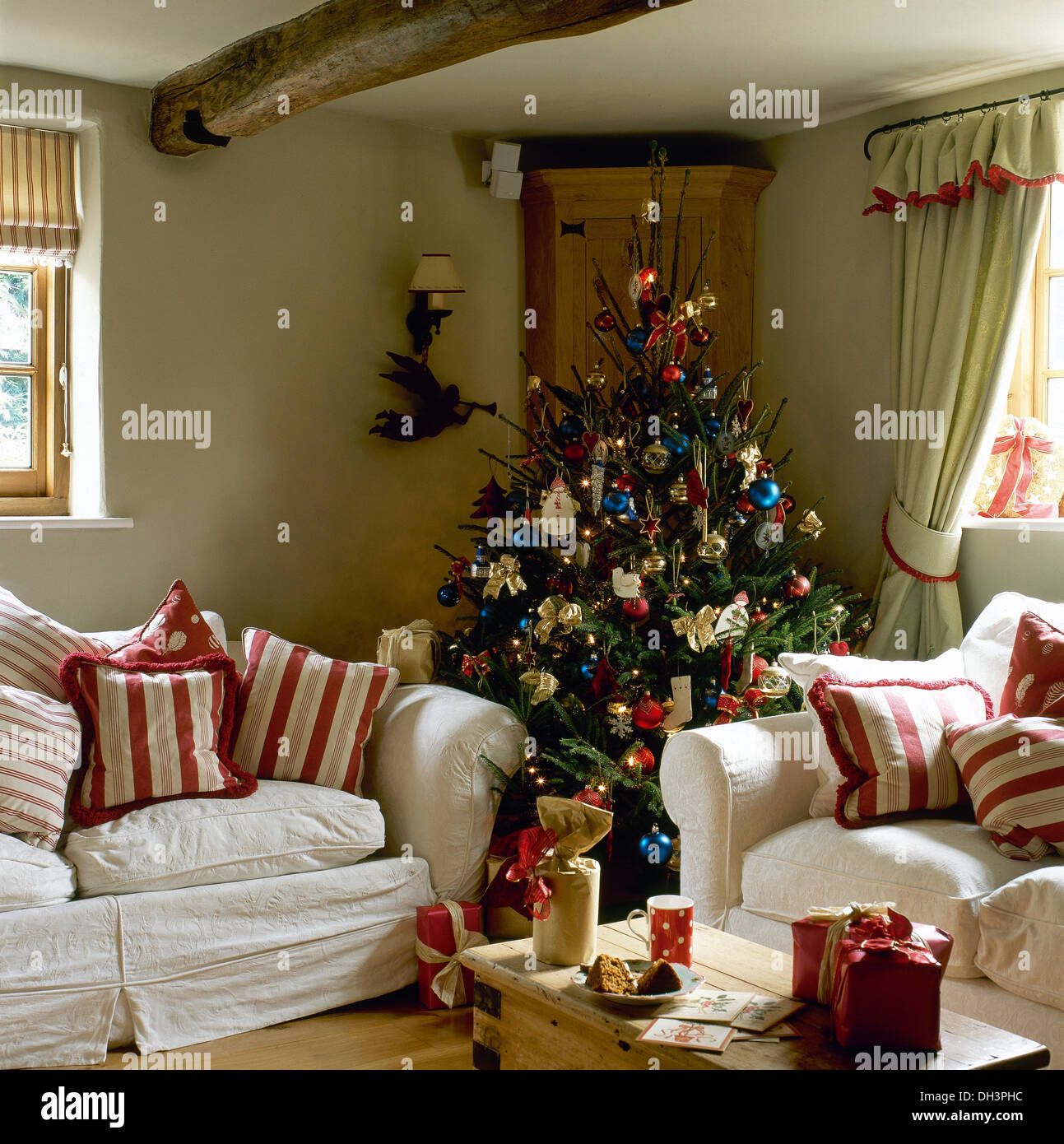 Albero di Natale decorato in angolo del cottage in salotto con strisce  rosse cuscini sui divani bianchi e i regali di Natale sul tavolo Foto stock  - Alamy