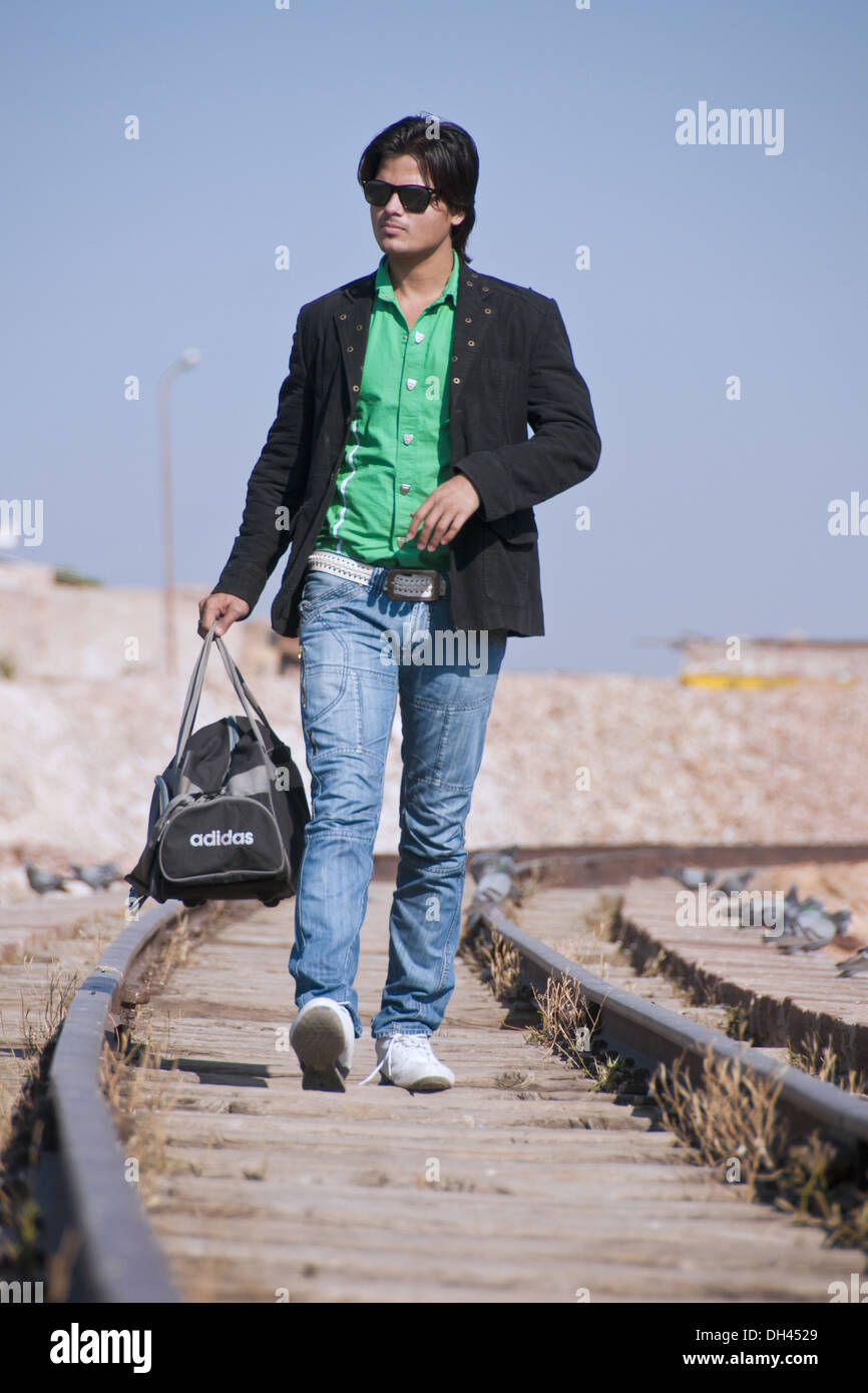 Uomo in blue jeans camicia bicchieri sacchetto contenitore camminando sul binario ferroviario Foto Stock