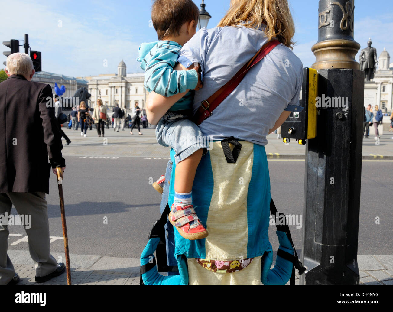 Londra, Inghilterra, Regno Unito. Trafalgar Square - donna che porta il suo figlio, in attesa di attraversare la strada Foto Stock