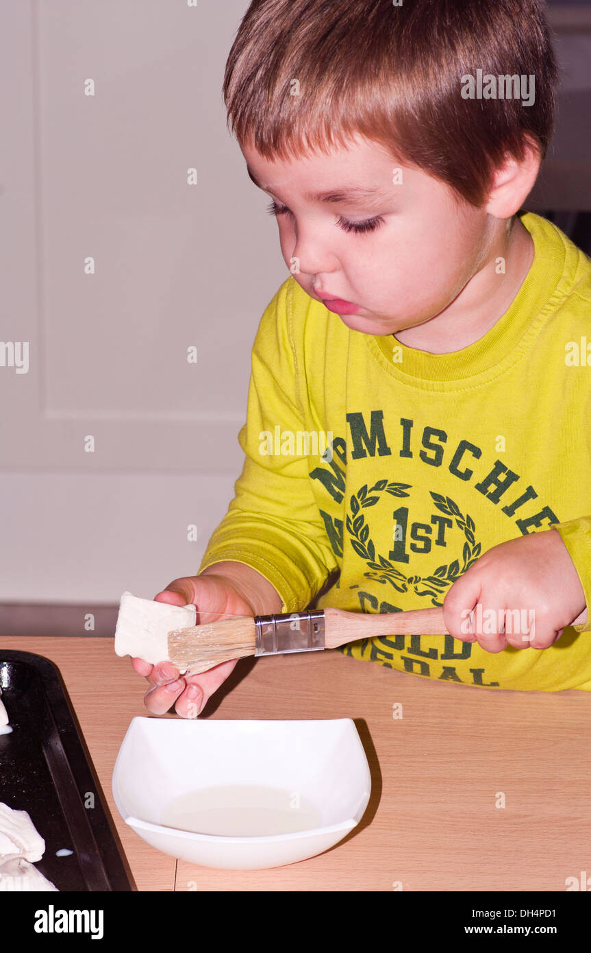 Little Boy aiutare in cucina con angolo cottura rendendo rotoli di salsiccia Foto Stock