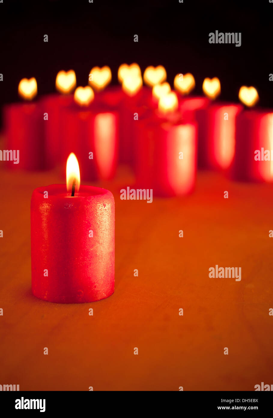 Candela rossa bruciare tranquillamente, con simili candele su sfondo con cuori di fiamme - simbolo della stagione di pace e di amore Foto Stock