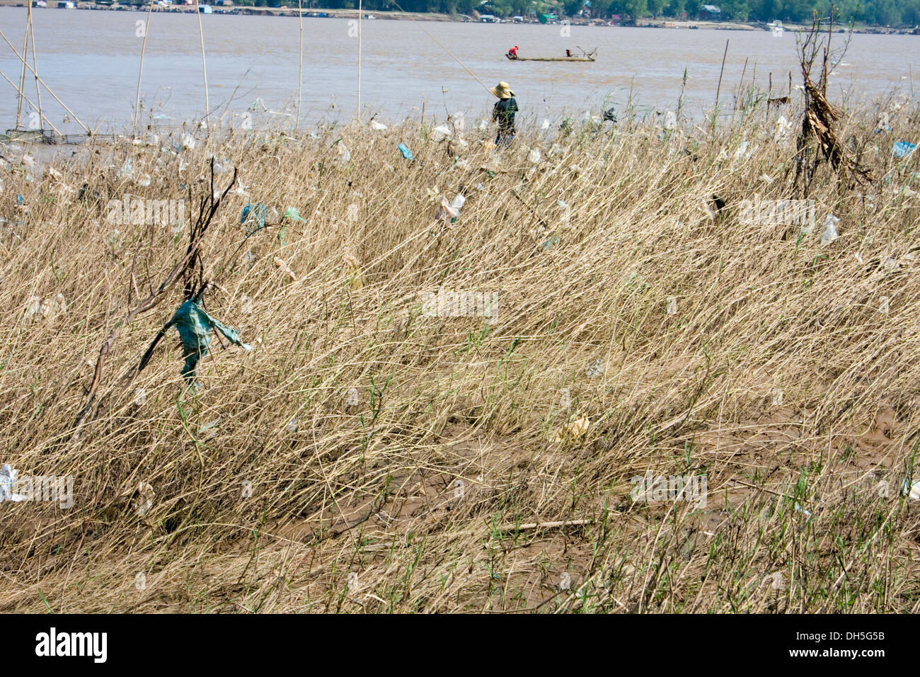 Un pescatore è la pesca nei pressi di sacchetti di plastica che sono raccolti in erbacce sulle rive del fiume Mekong in Kampong Cham, Cambogia. Foto Stock