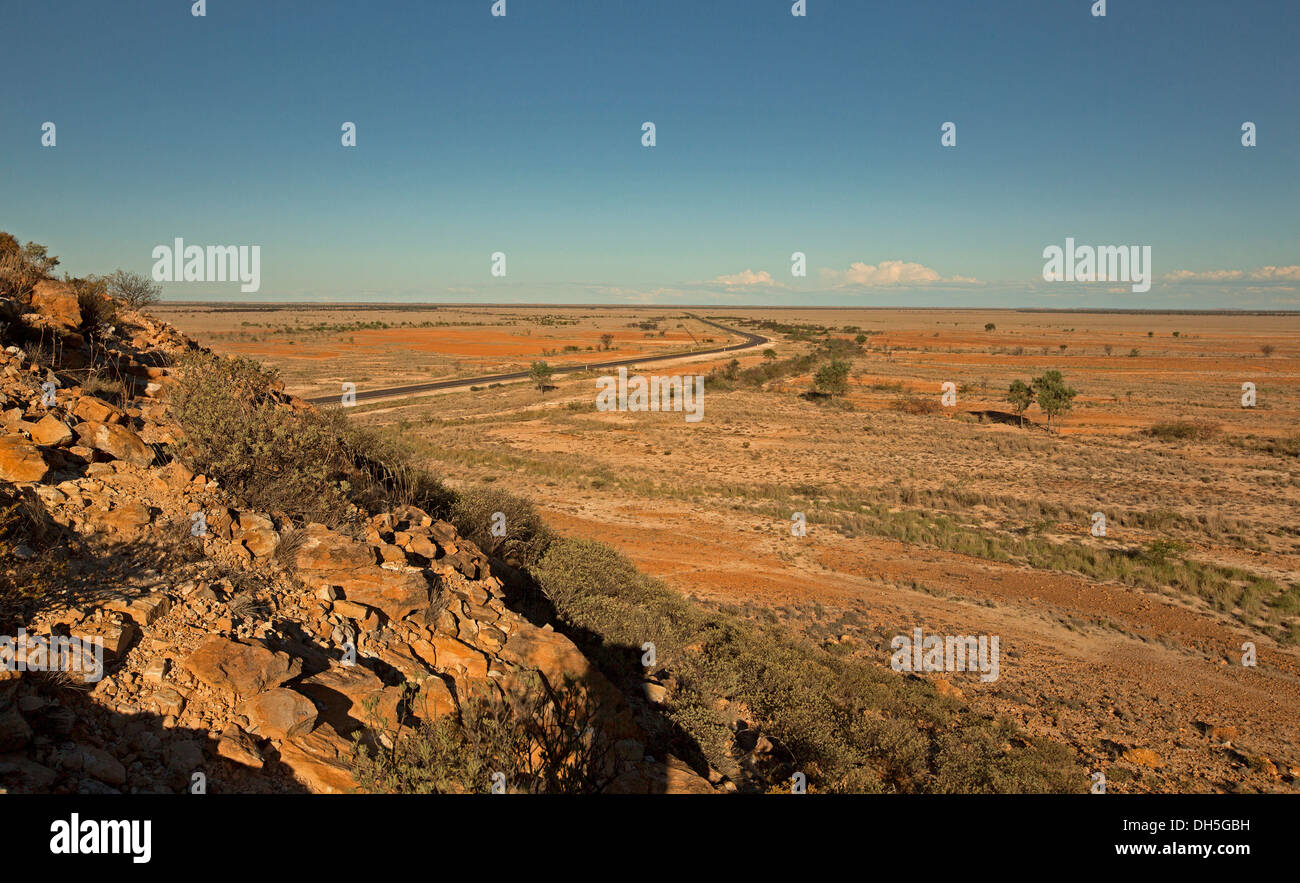 Vasto arido entroterra australiano di paesaggio con road per affettare tutta pianura brulla allungamento lontano orizzonte in western Queensland durante la siccità Foto Stock