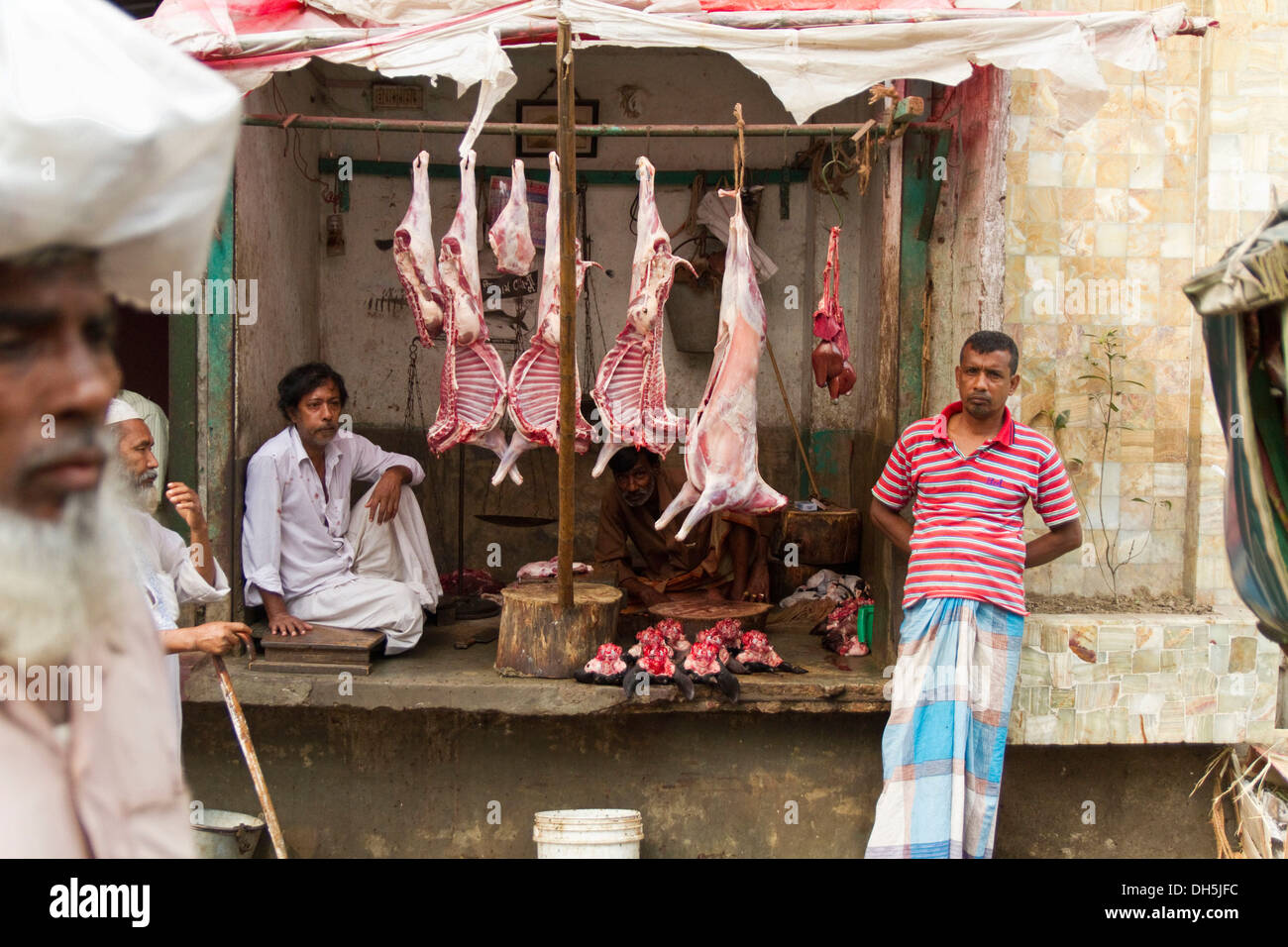 Macello stradale, scuoiati animali appesi da travi, carne cruda al di sotto del macellaio di attesa per i clienti, Dhaka Foto Stock