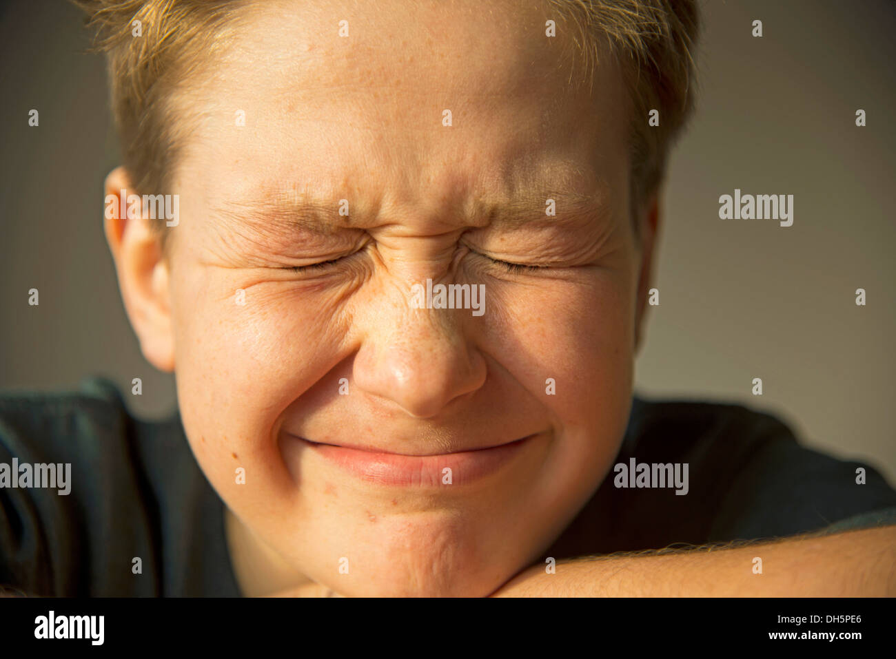 Ragazzo di dodici anni strizzare gli occhi i suoi occhi, primi segni di acne sul viso, pubertà, Germania Foto Stock
