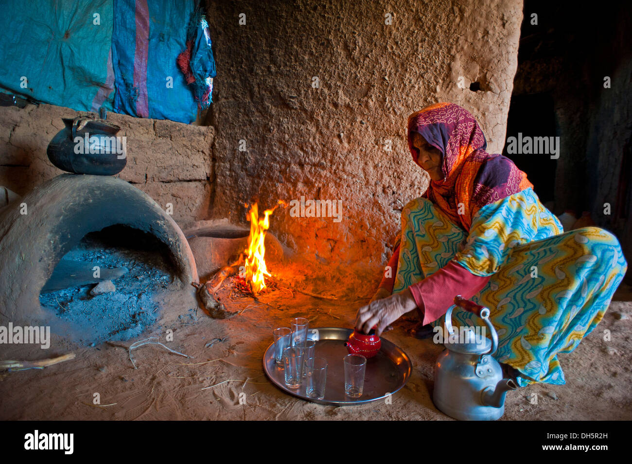 Anziana donna berbera preparando il tè mentre accovacciata sul terreno di fronte a un forno di argilla e un incendio di piccole dimensioni, Erg Chebbi Foto Stock