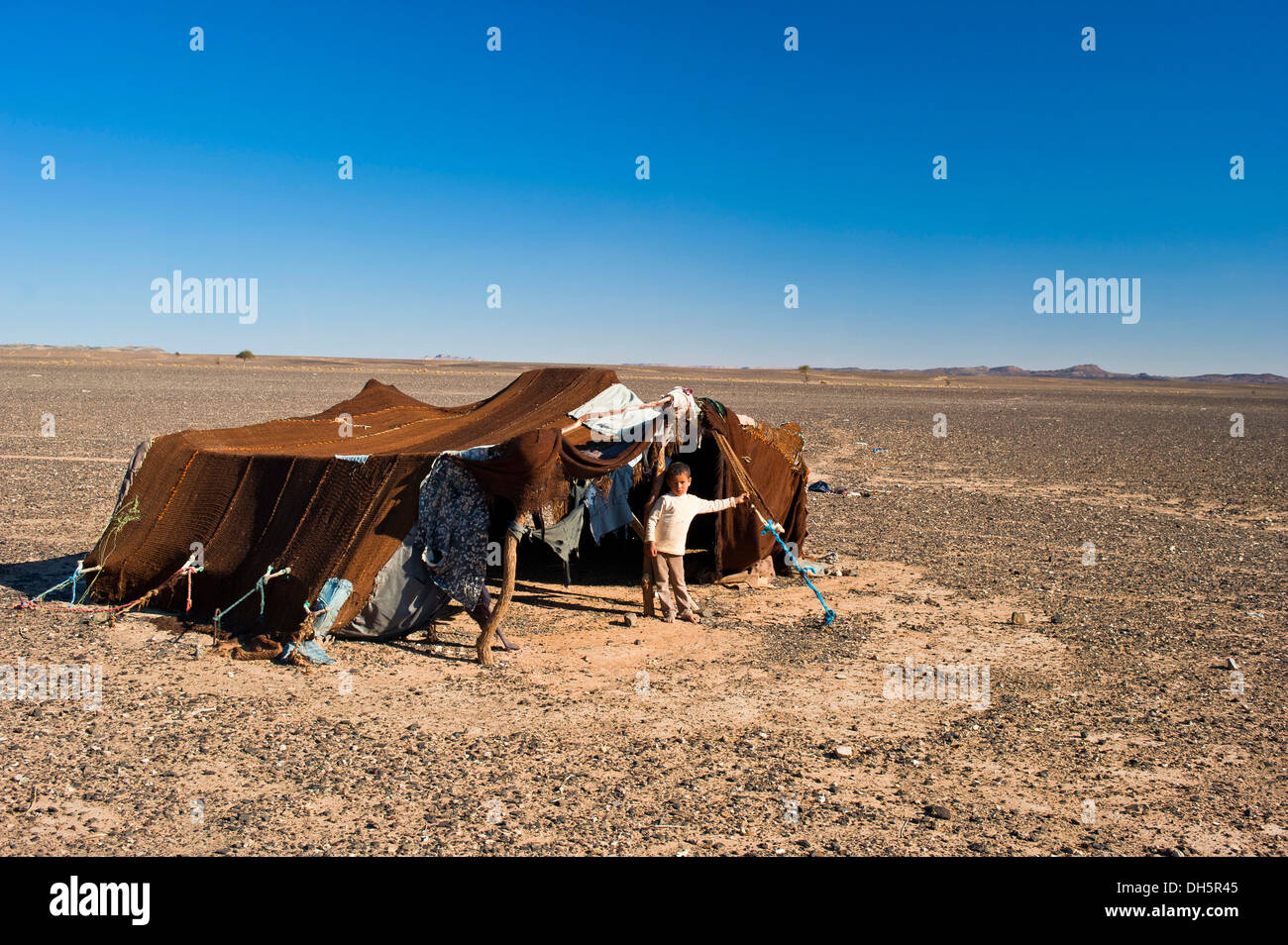 Giovane ragazzo in piedi nella parte anteriore della tenda della sua famiglia nomade, deserto di pietra, hamada, Erg Chebbi, sud del Marocco, Marocco Foto Stock