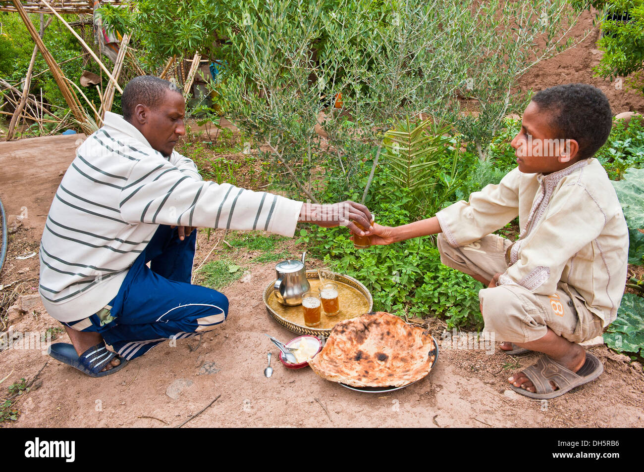Un riff uomo si consegna a un bicchiere di tè alla menta ad un ragazzo, sul terreno ci è piatto pane burro e un vassoio di ottone con teiera e Foto Stock