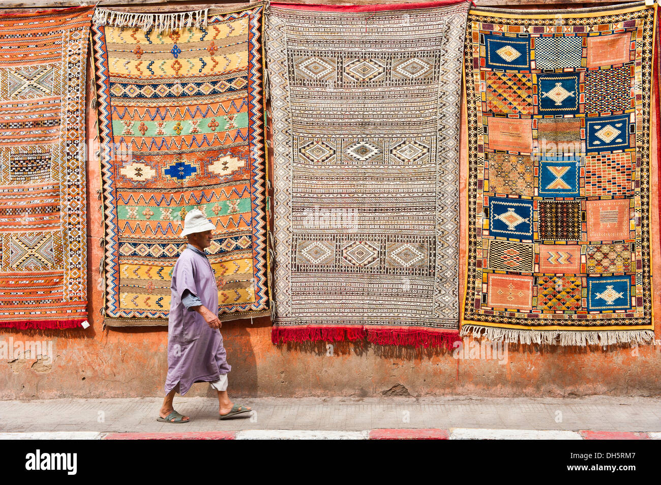 Moquette o tappeti con gli arabi e i simboli di Berbera e modelli, appeso a una facciata per vendita, uomo anziano in una djellabah passato a piedi Foto Stock