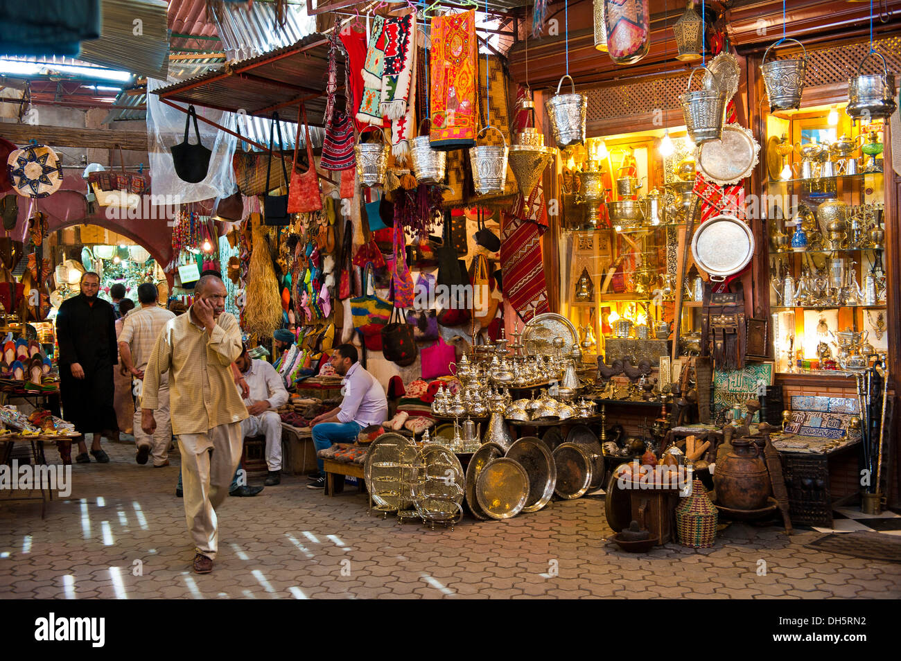 La gente camminare passato i negozi per la vendita di merci in ottone e tessuti in un vicoletto nei souks, area bazaar, Marrakech, Marocco, Africa Foto Stock