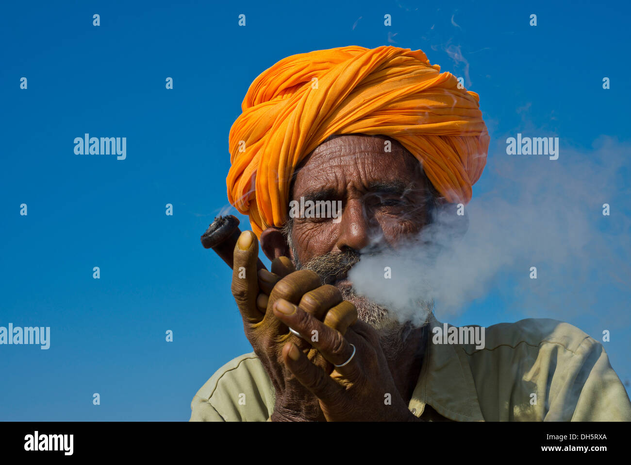 Rajasthani anziani uomo con un turban arancione fumare una tubazione di hash o hooka Kamelmarkt,,,, Pushkar Rajasthan, India Foto Stock