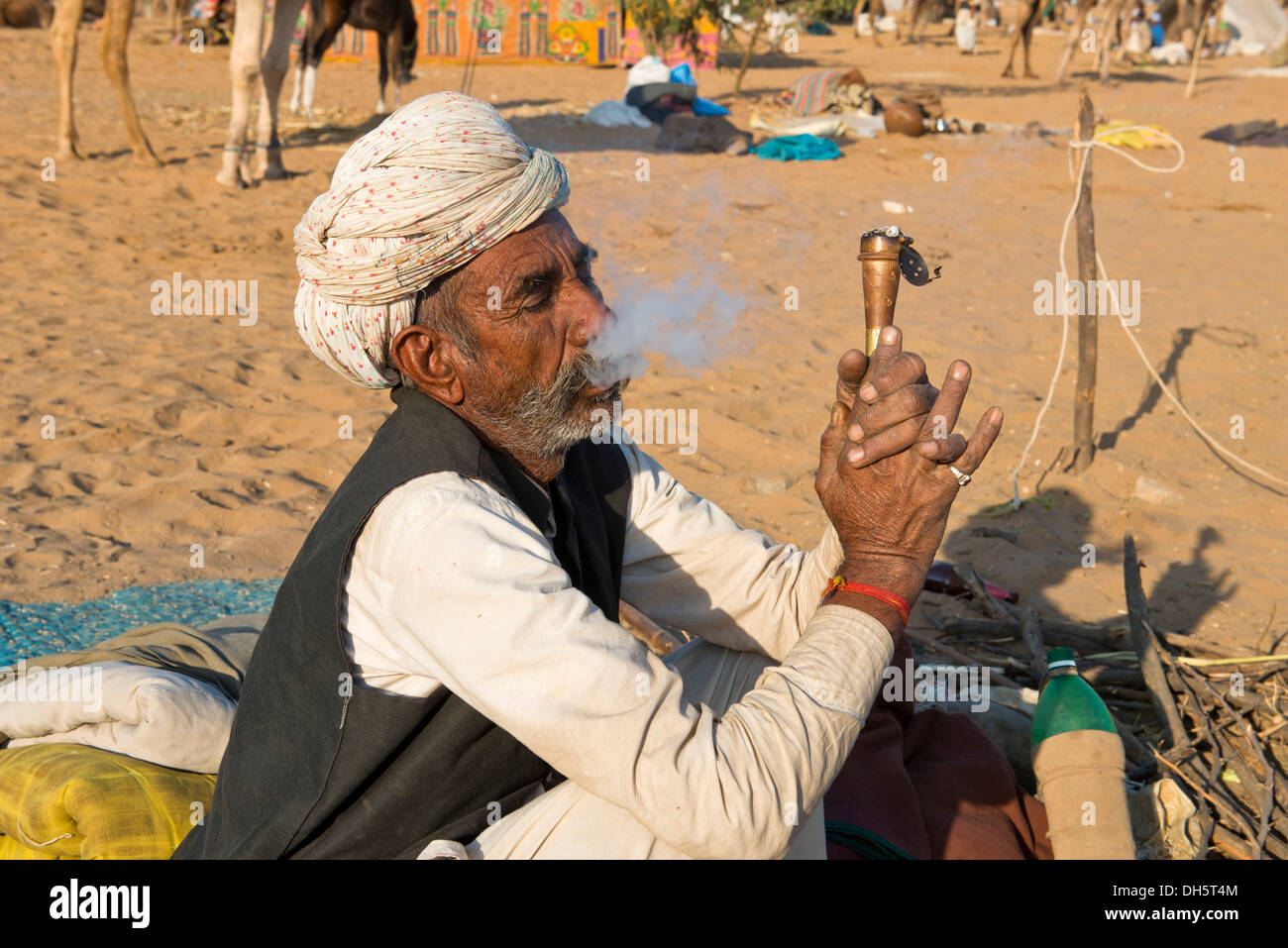 Indiano con un turbante seduto per terra fumare una tubazione di hash, Pushkar Camel Fair, Pushkar, Rajasthan, India Foto Stock