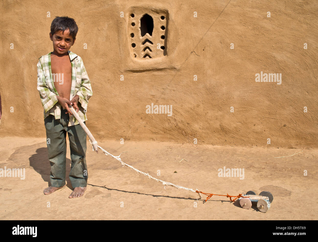 Ragazzo giocando con un giocattolo auto al di fuori di una casa di fango, Wüste Thar, Rajasthan, India Foto Stock
