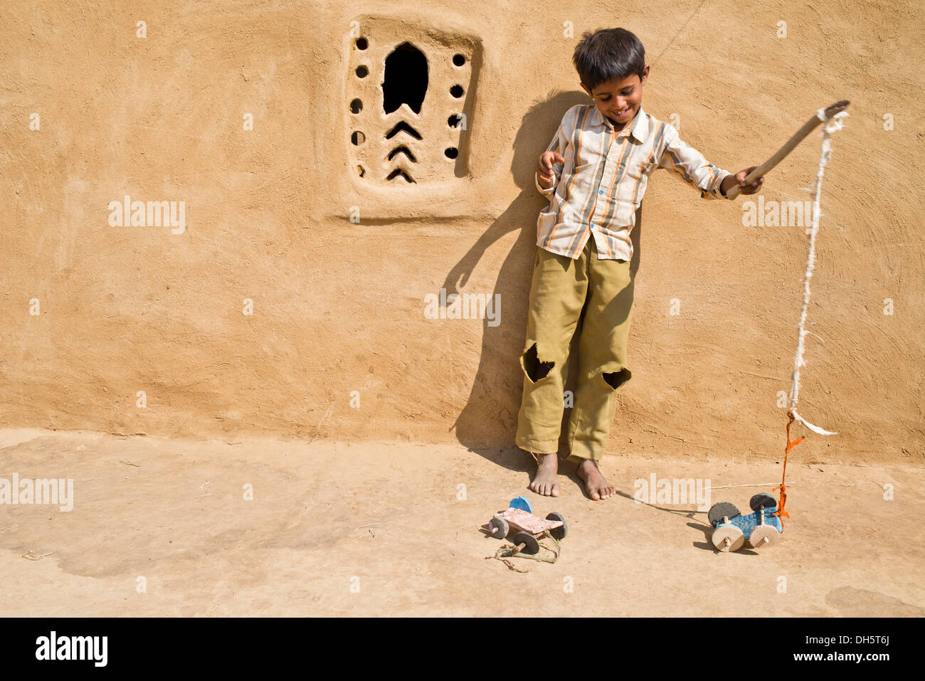 Ragazzo giocando con un giocattolo auto al di fuori di una casa di fango, Wüste Thar, Rajasthan, India Foto Stock