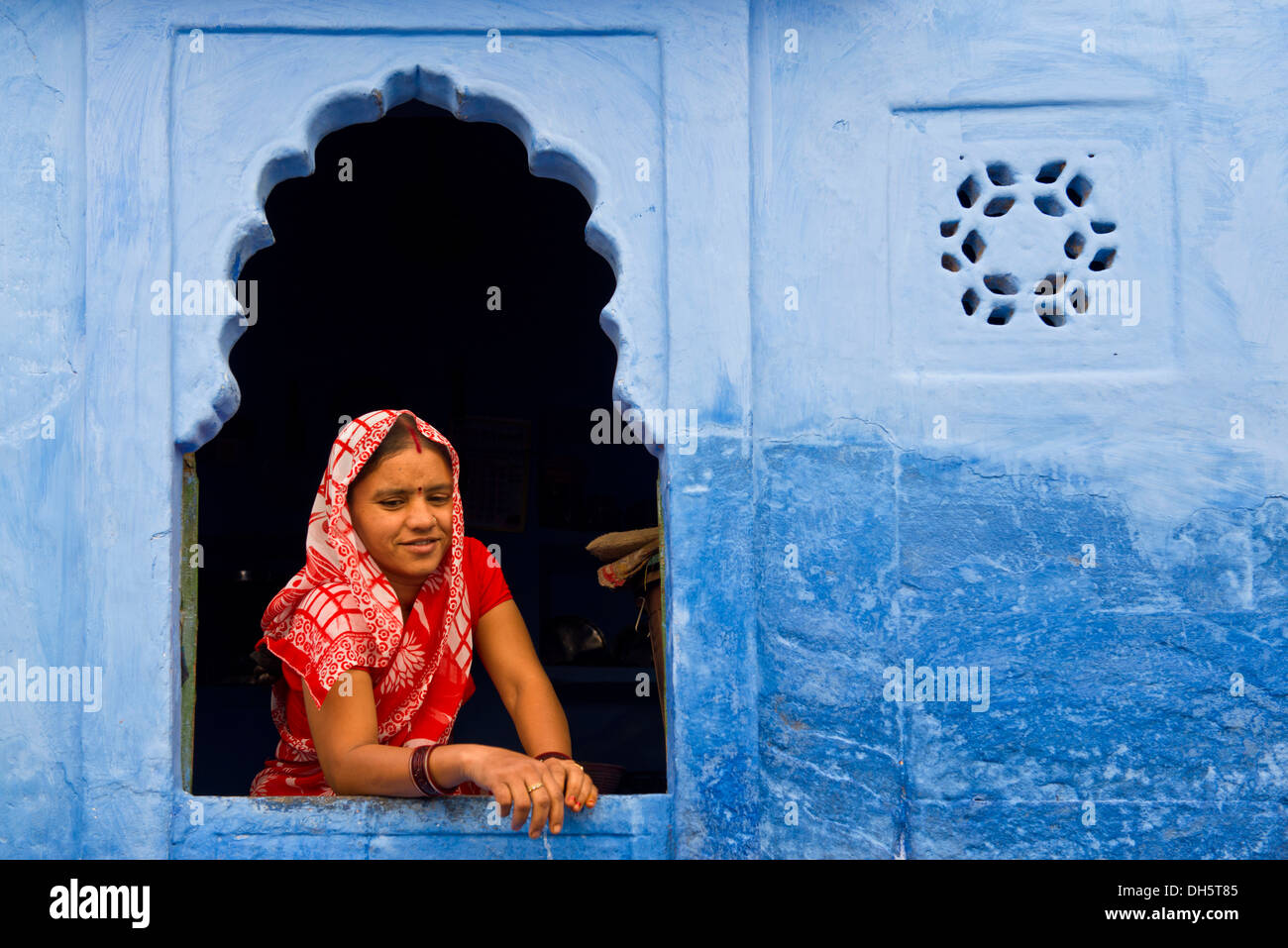 Giovane donna indiana con velo guardando fuori dalla finestra di un blu casa residenziale, Jodhpur, Rajasthan, India Foto Stock