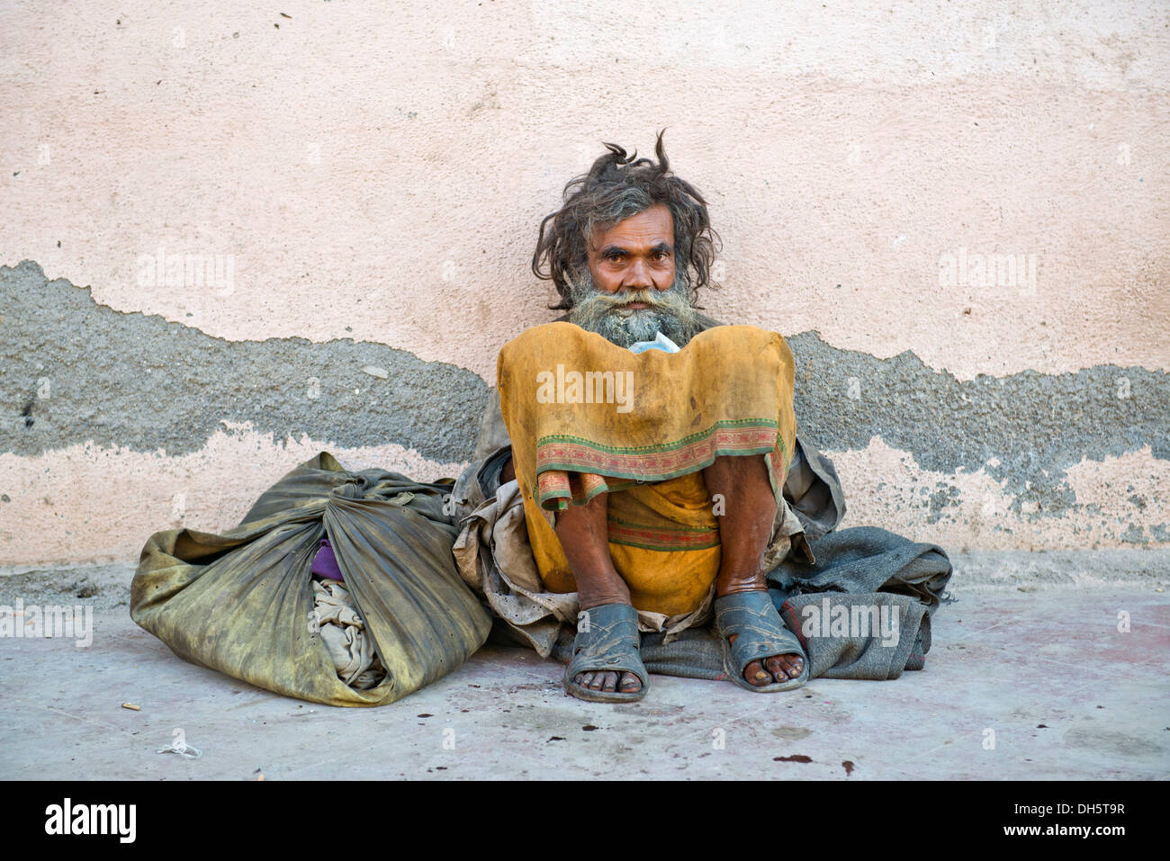 Beggar appoggiata contro un muro di casa, seduti, Orchha, Madhya Pradesh, India Foto Stock