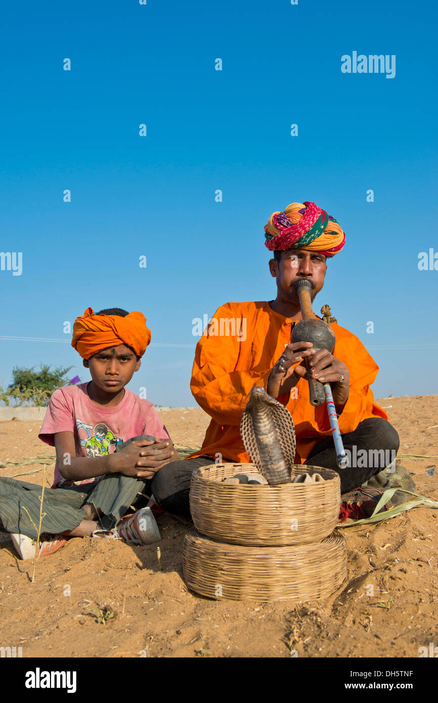 Rajasthani incantatore di serpente con un turbante, riproduzione di un flauto, un cobra o Naja avvolgimento da un cestello davanti a lui Foto Stock