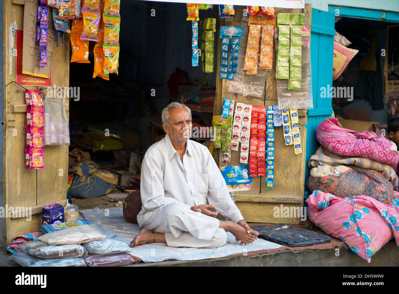 Senior Indian uomo seduto su una coperta di fronte al suo stallo, Jodhpur, Rajasthan, India Foto Stock