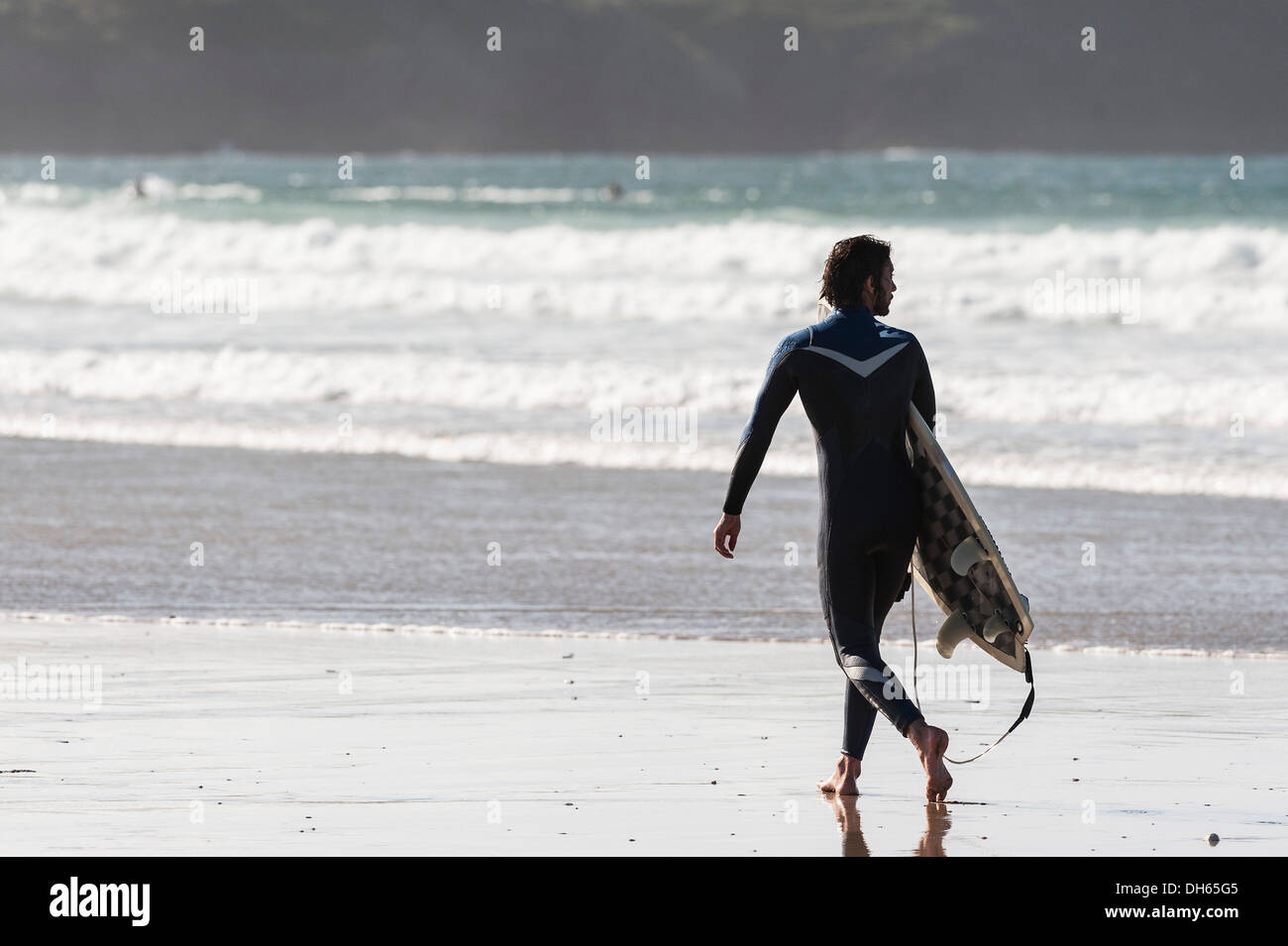 Un surfista maschio camminando lungo il litorale su Fistral Beach in Newquay. Foto Stock