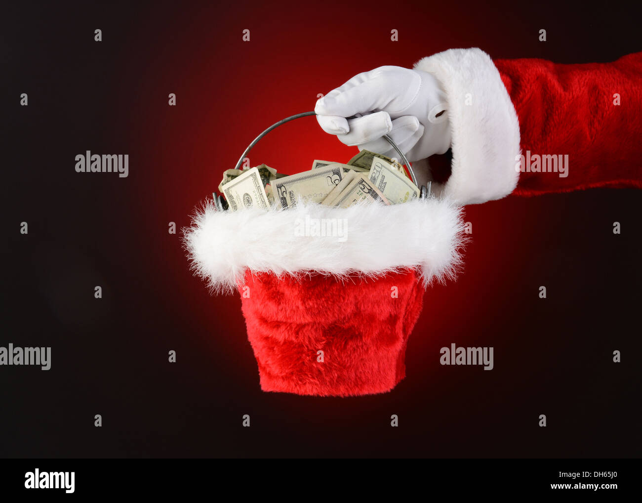 Primo piano di Santa Claus tenendo un secchio di contanti. Solo Santa la mano e il braccio su una luce di colore rosso scuro dello sfondo. Foto Stock