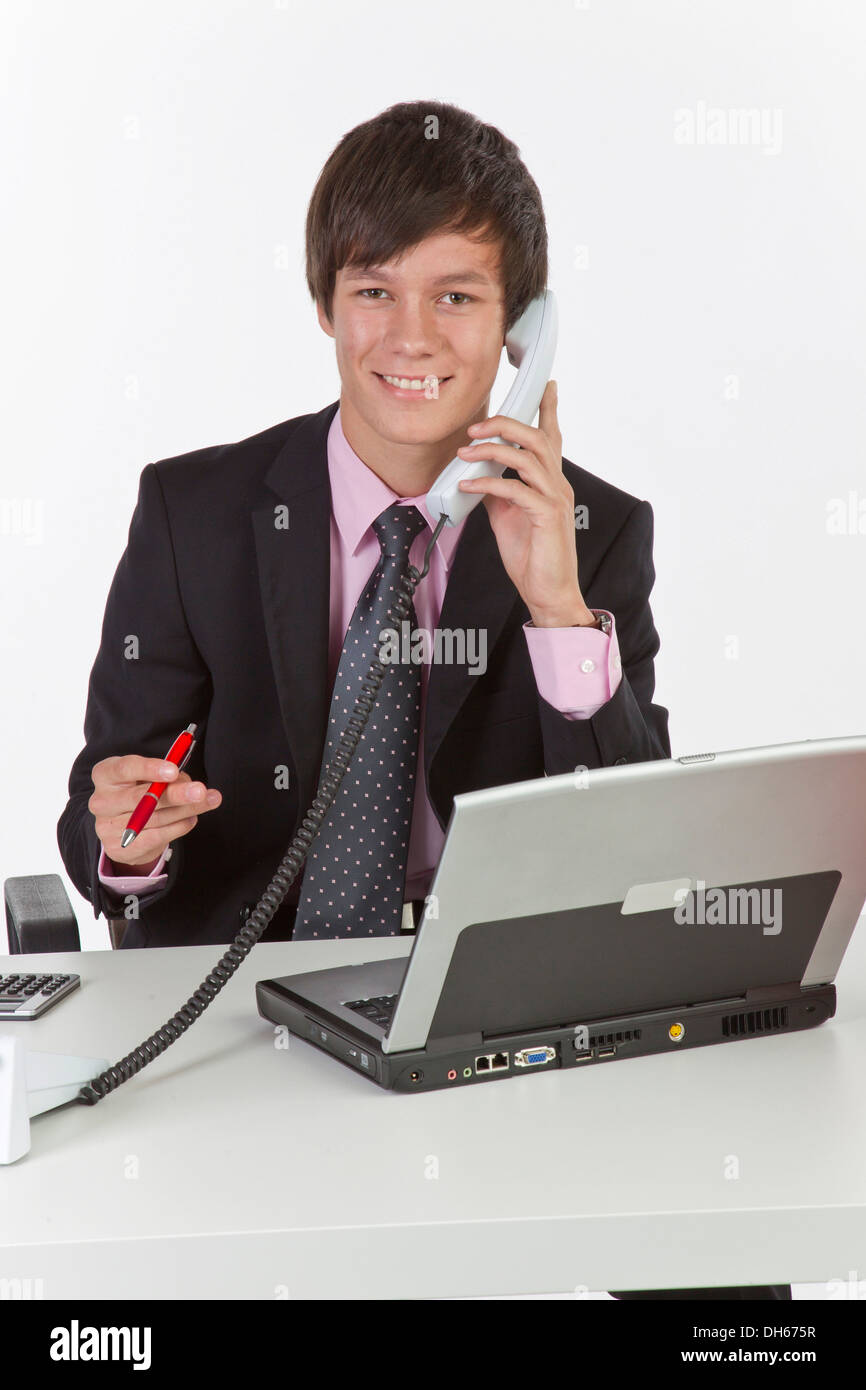 Giovane uomo seduto a un computer portatile e in possesso di un telefono cellulare Foto Stock