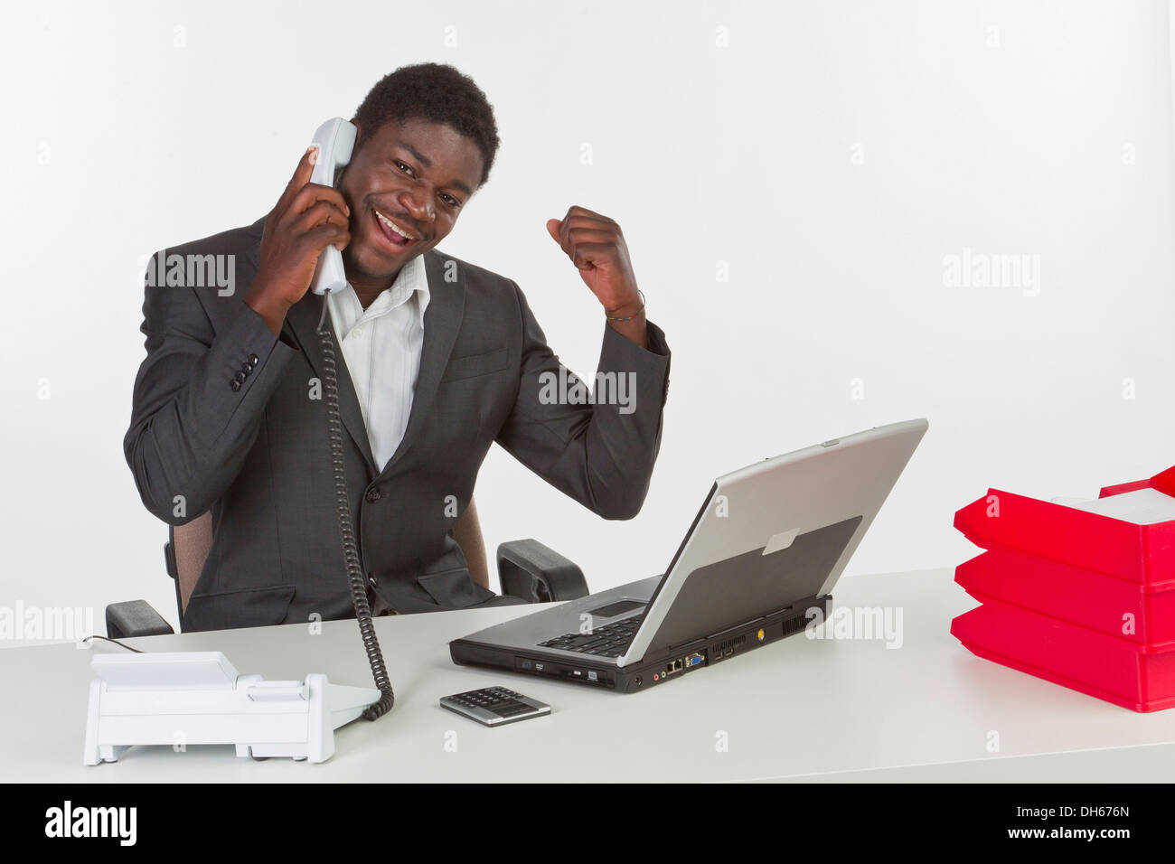 I giovani di carnagione scura uomo seduto a un computer portatile e di tenere un telefono mentre cercando felice Foto Stock