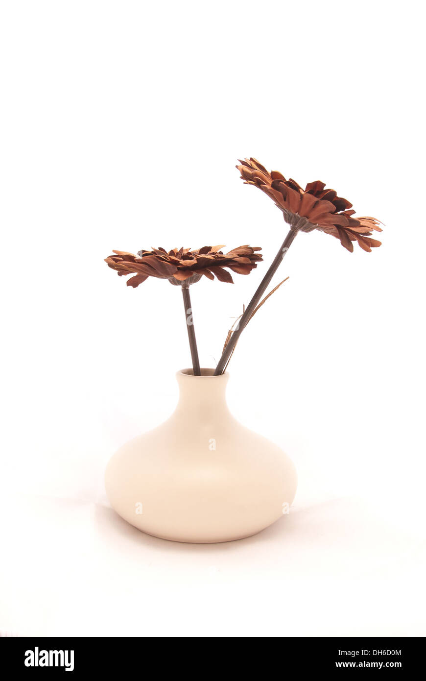 Una coppia di marrone margherite artificiale in un moderno, avorio vaso in ceramica su un panno bianco Foto Stock